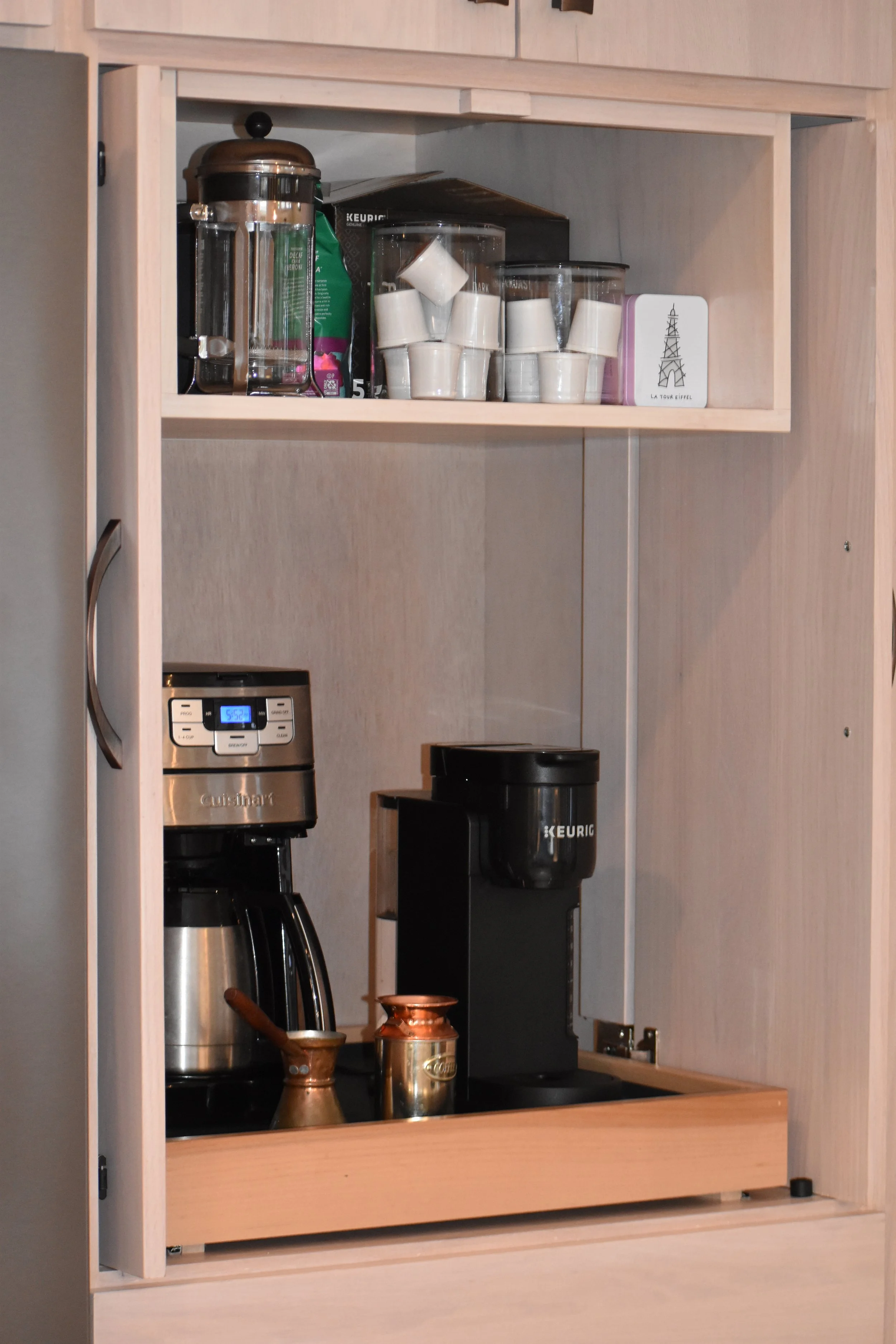 Inside a wooden kitchen cabinet with coffee-making appliances and supplies, including a coffee machine, a Keurig coffee maker, cups, and utensils. Marietta GA kitchen remodel.