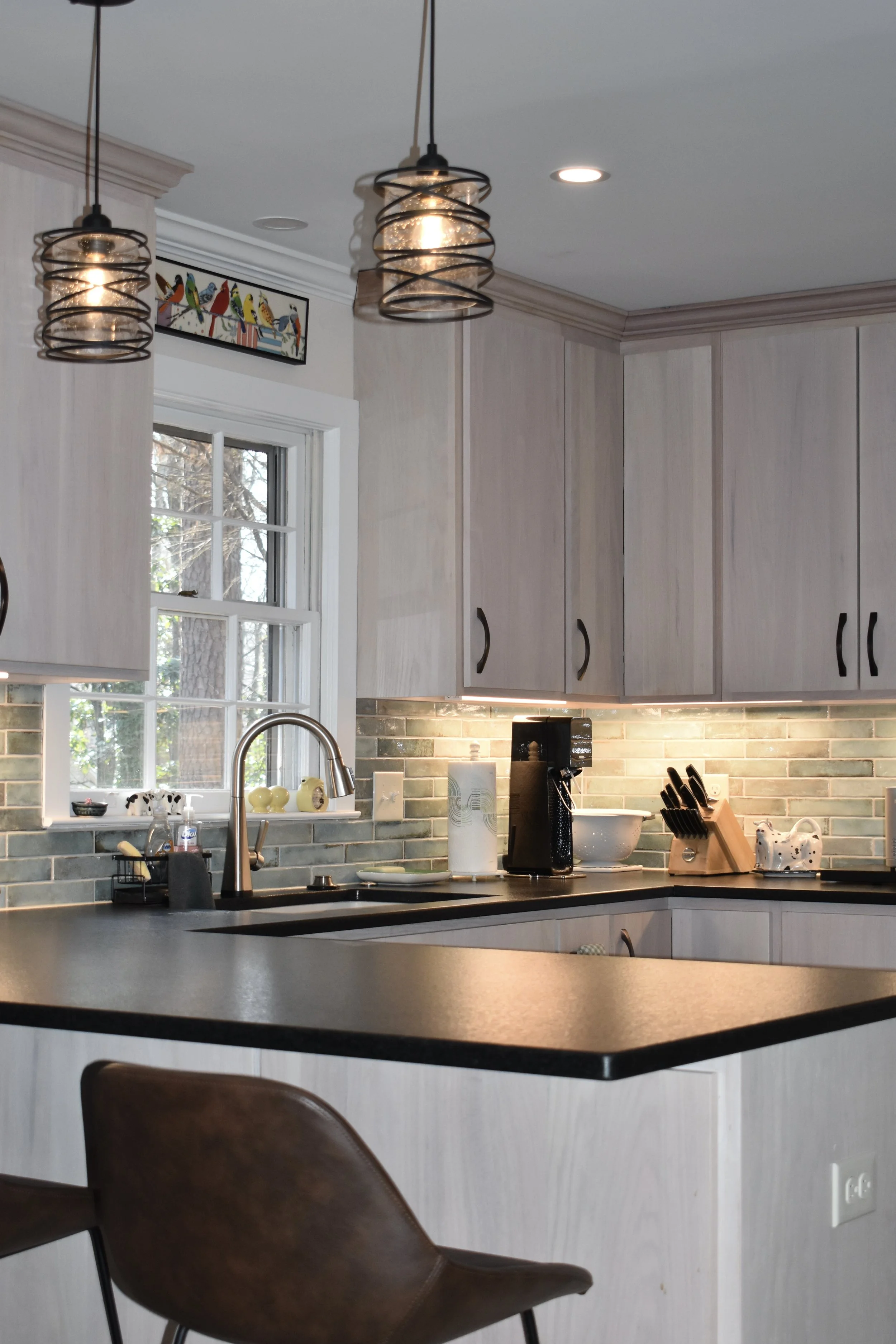 A modern kitchen with white cabinetry, pendant lights, a window above the sink, and various kitchen appliances and utensils on the countertop. Marietta GA kitchen remodel.
