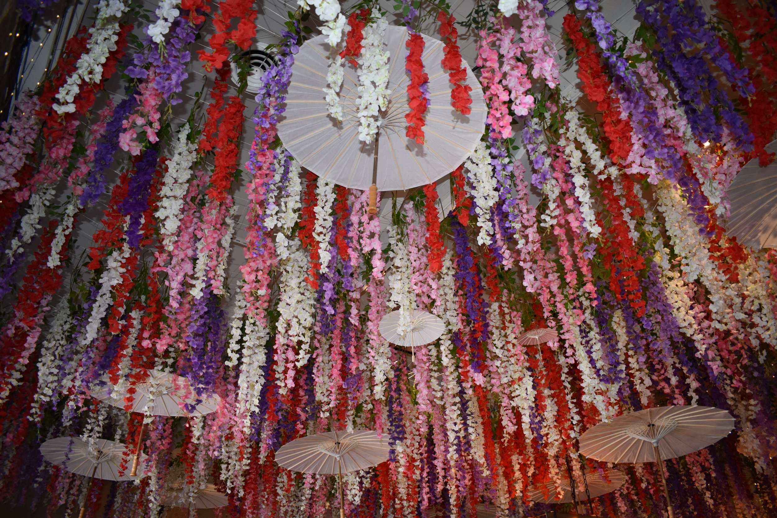 Ceiling decorated with hanging colorful flowers and white paper umbrellas. Hamp & Harry's Marietta Square.