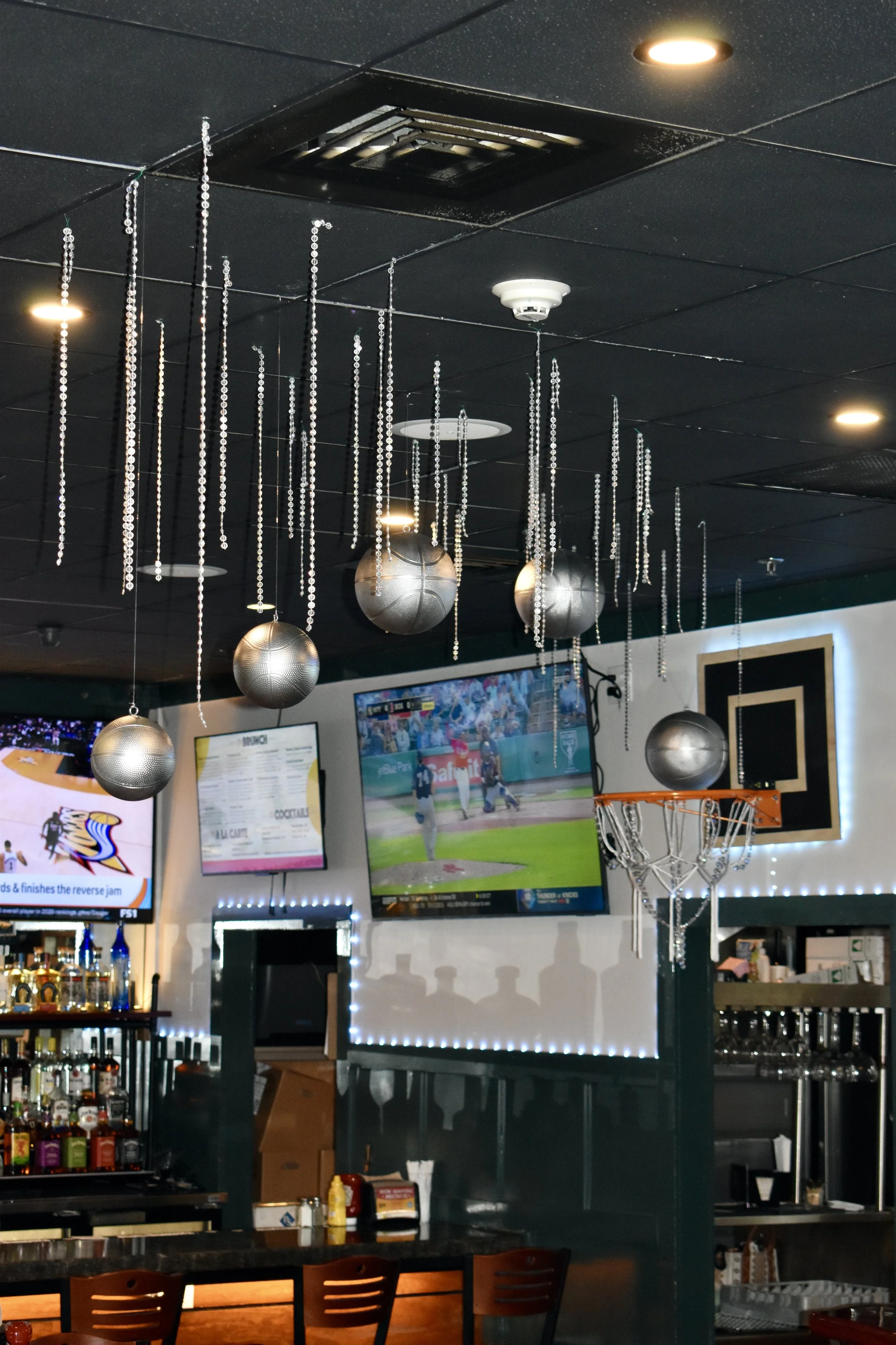 Interior of a sports bar with a basketball hoop, hanging silver basketball-themed decorations, and multiple TVs showing sports events. March Madness
