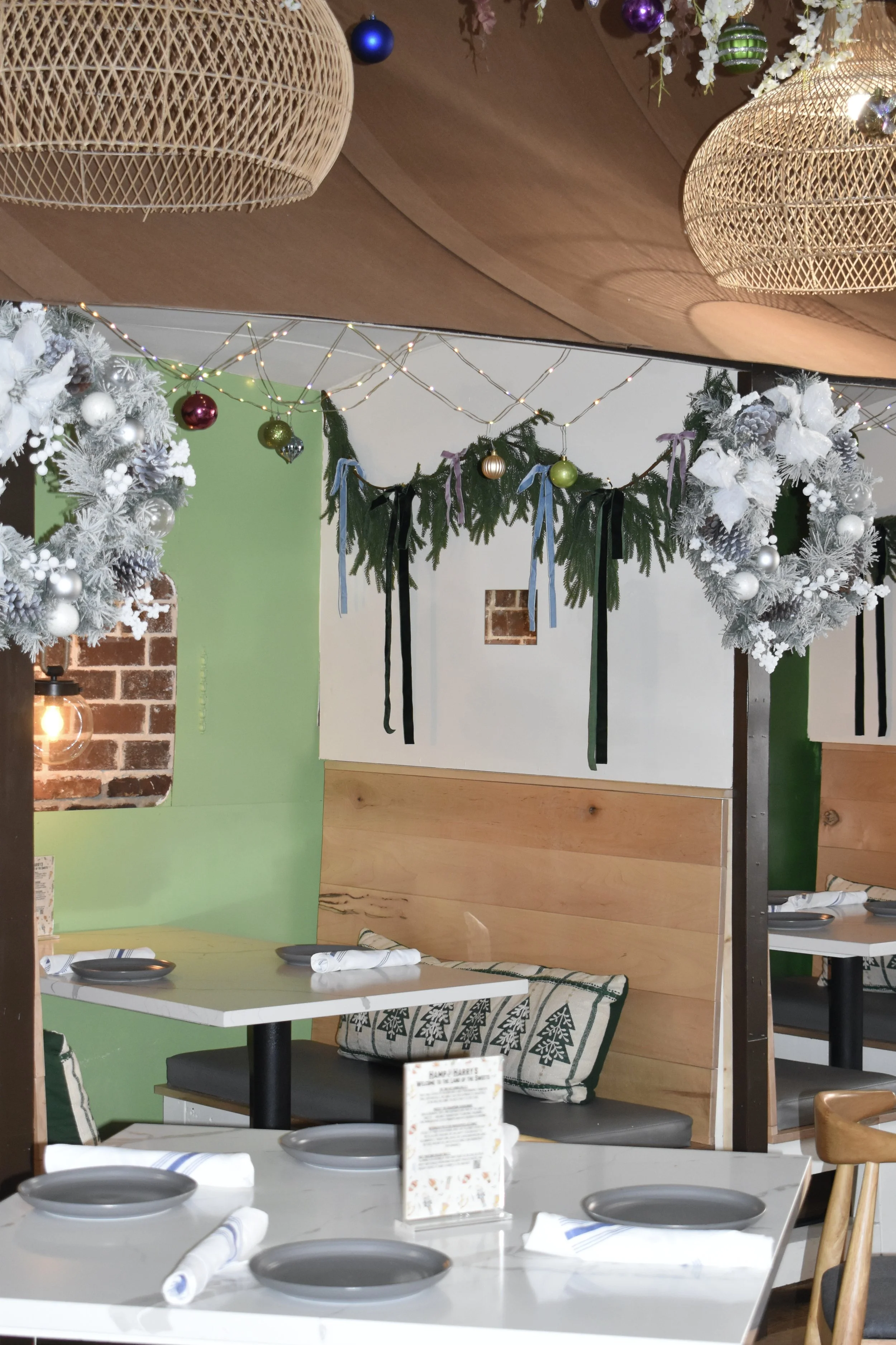 Decorated dining area with Christmas wreaths, garland, and hanging ornaments, featuring tables set with plates and napkins.