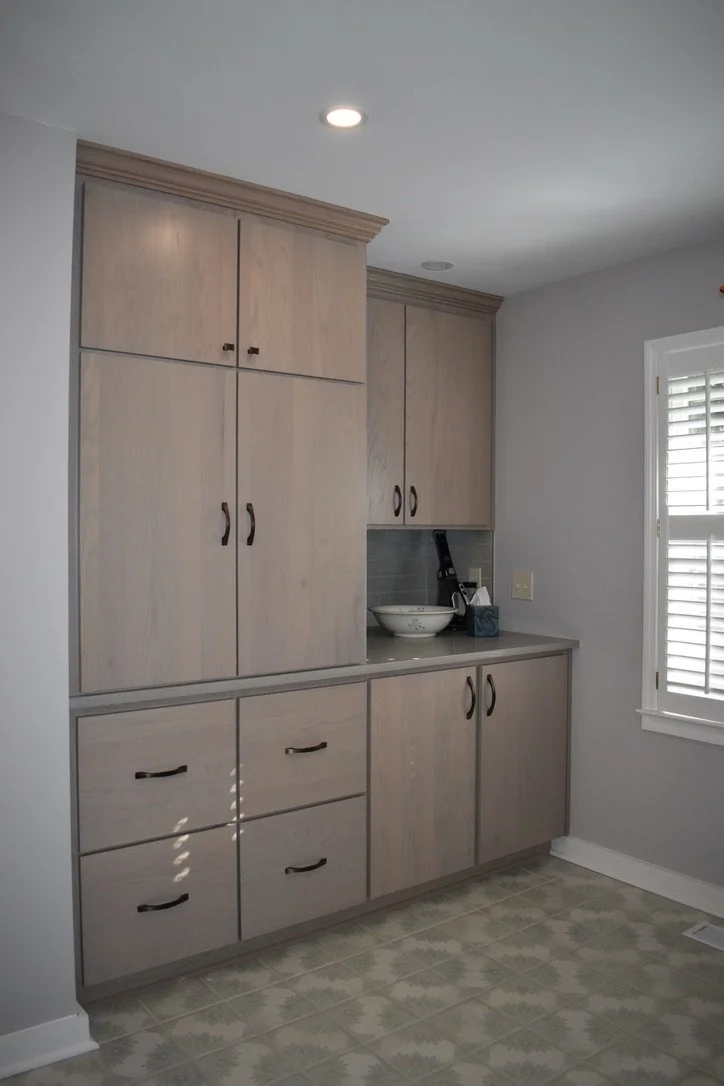 Kitchen with light wood cabinets, gray countertop, and white window shutters.