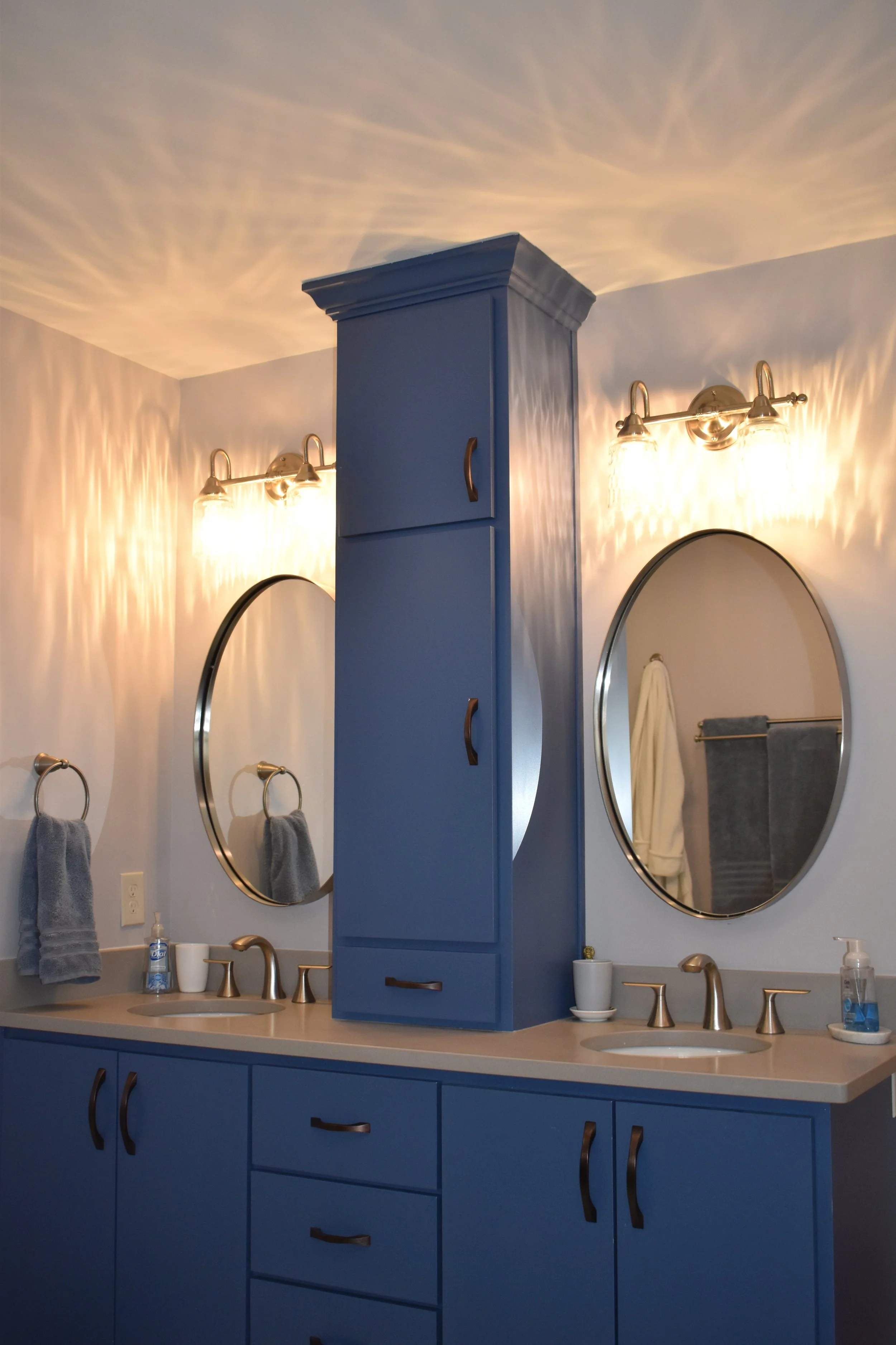 Bathroom with blue cabinets, two oval mirrors, and warm lighting. Marietta GA bathroom remodel.