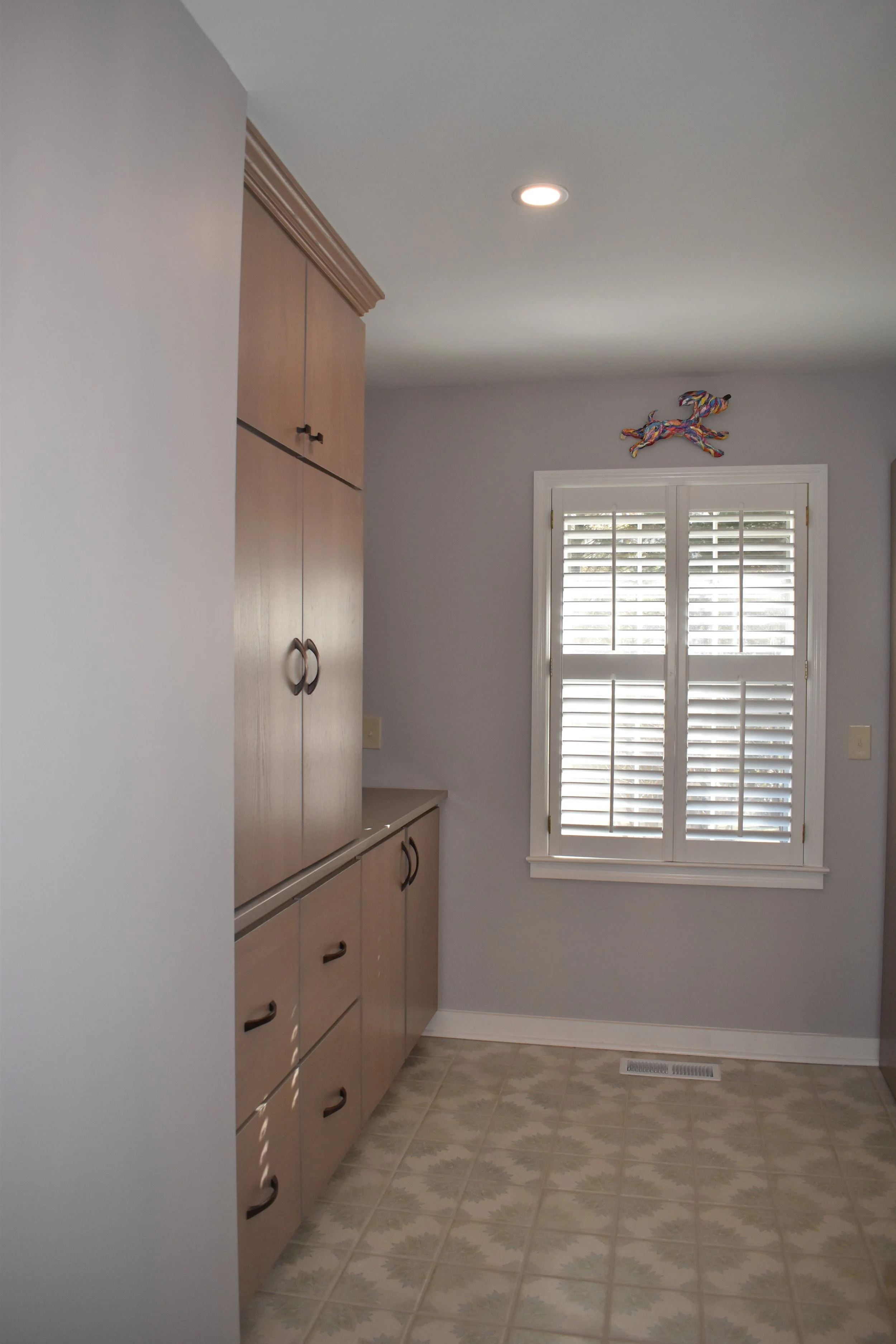 A room with a wooden cabinet and a window with white shutters, decorated with a colorful hanging horse figure at the top. Marietta GA bathroom remodel.