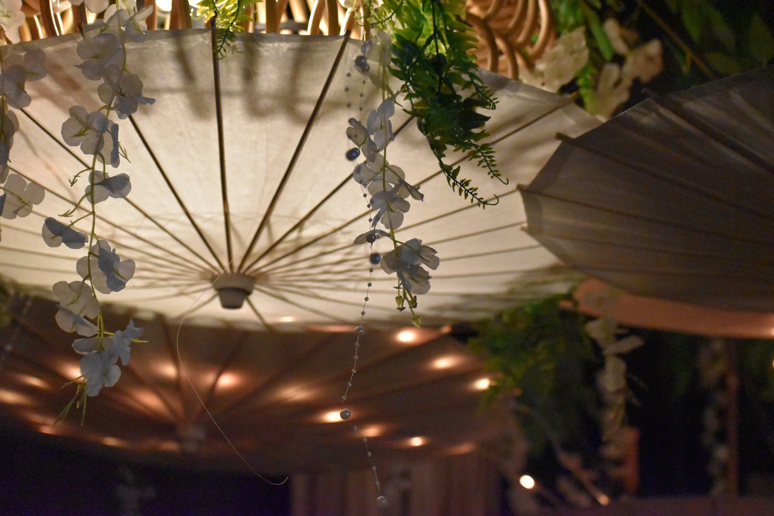 Decorative paper lanterns with floral and greenery embellishments hanging in a dark setting. Hamp & Harry's Marietta Square.