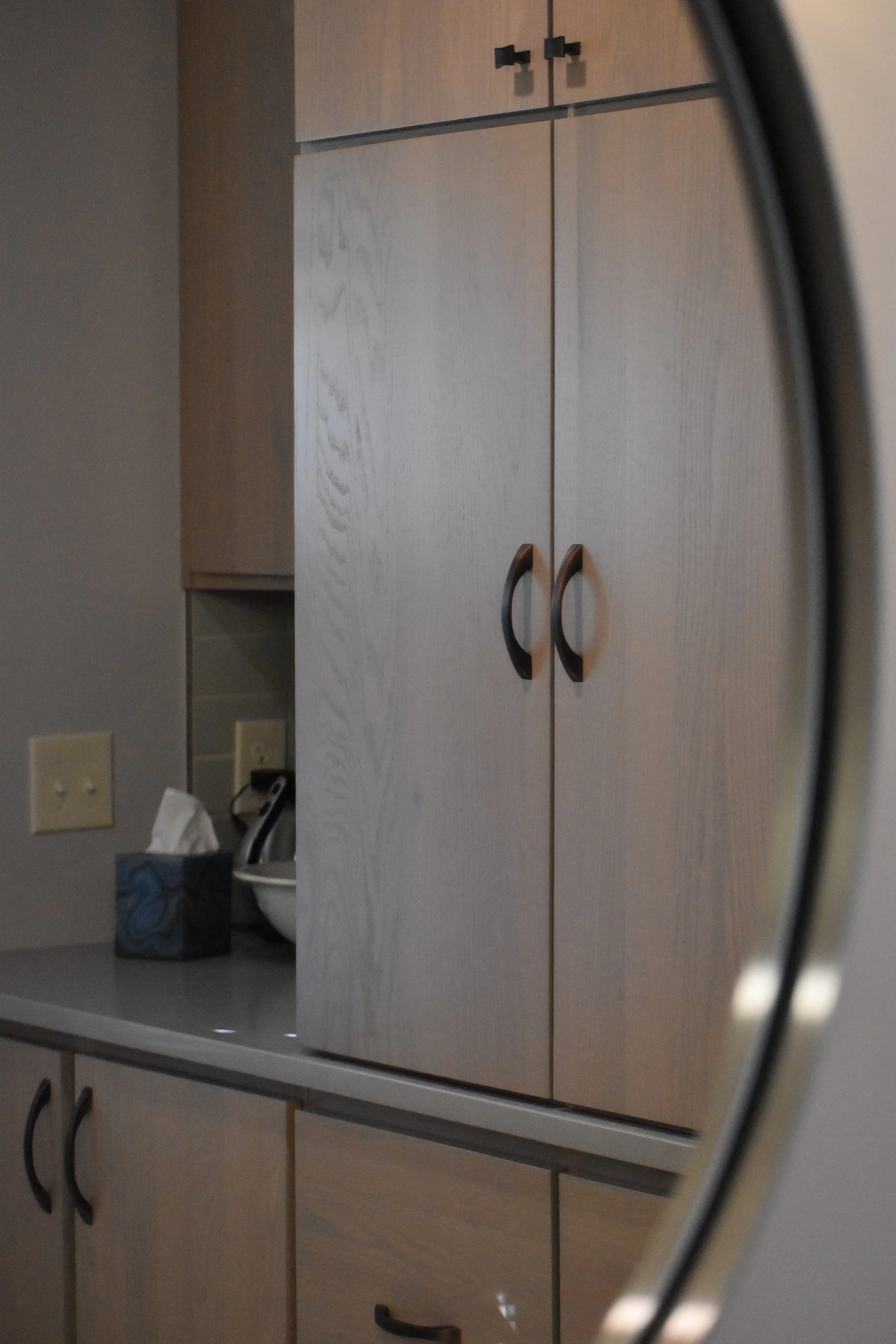 Kitchen cabinet reflected in a mirror, with tissues and a small kitchen appliance on the countertop. Marietta GA bathroom remodel.