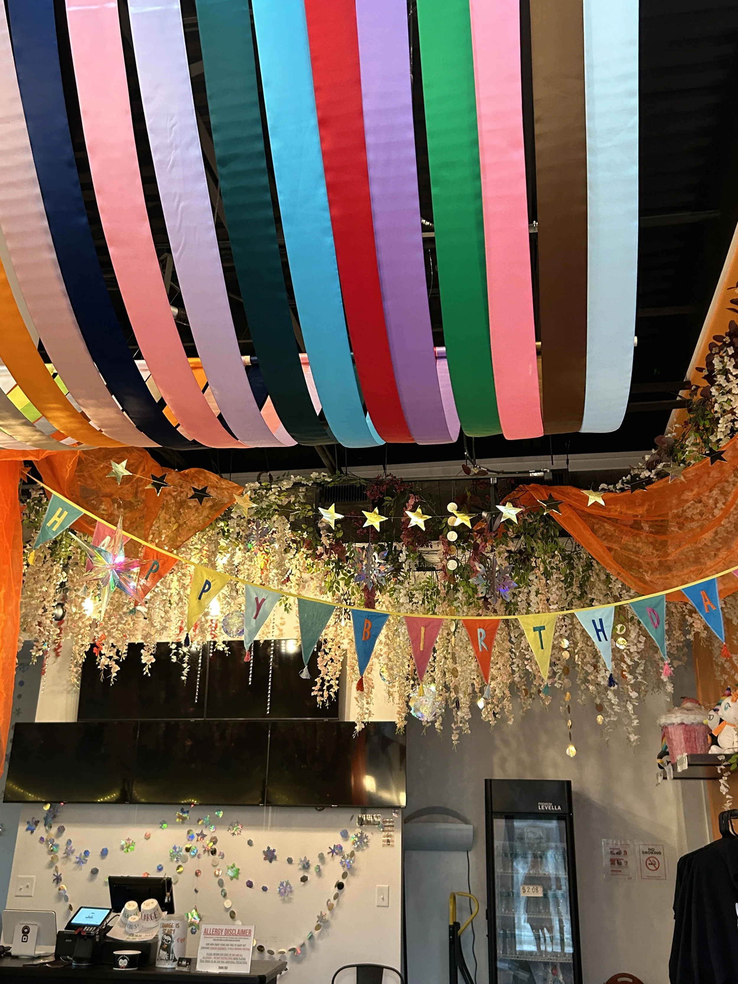 Colorful ceiling decorations hanging from the ceiling with a 'Happy Birthday' banner and floral decorations in the background.