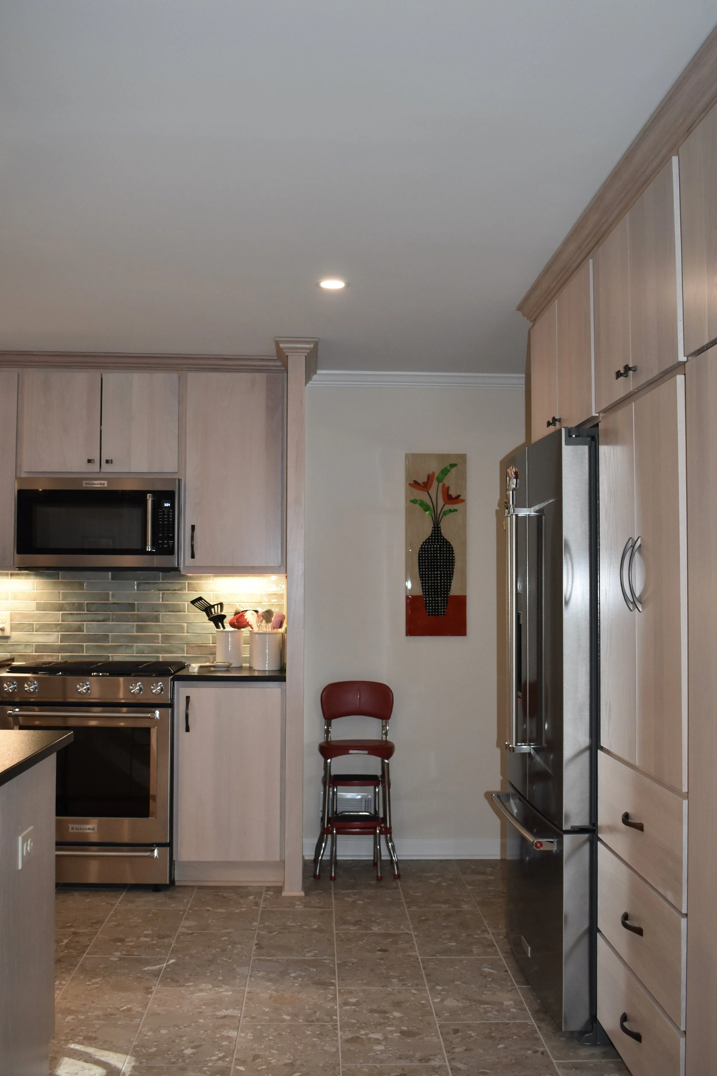 Interior view of a modern kitchen with wooden cabinets, stainless steel appliances, a painting of flowers on the wall, and a red chair stacked with another chair. Marietta GA kitchen remodel.