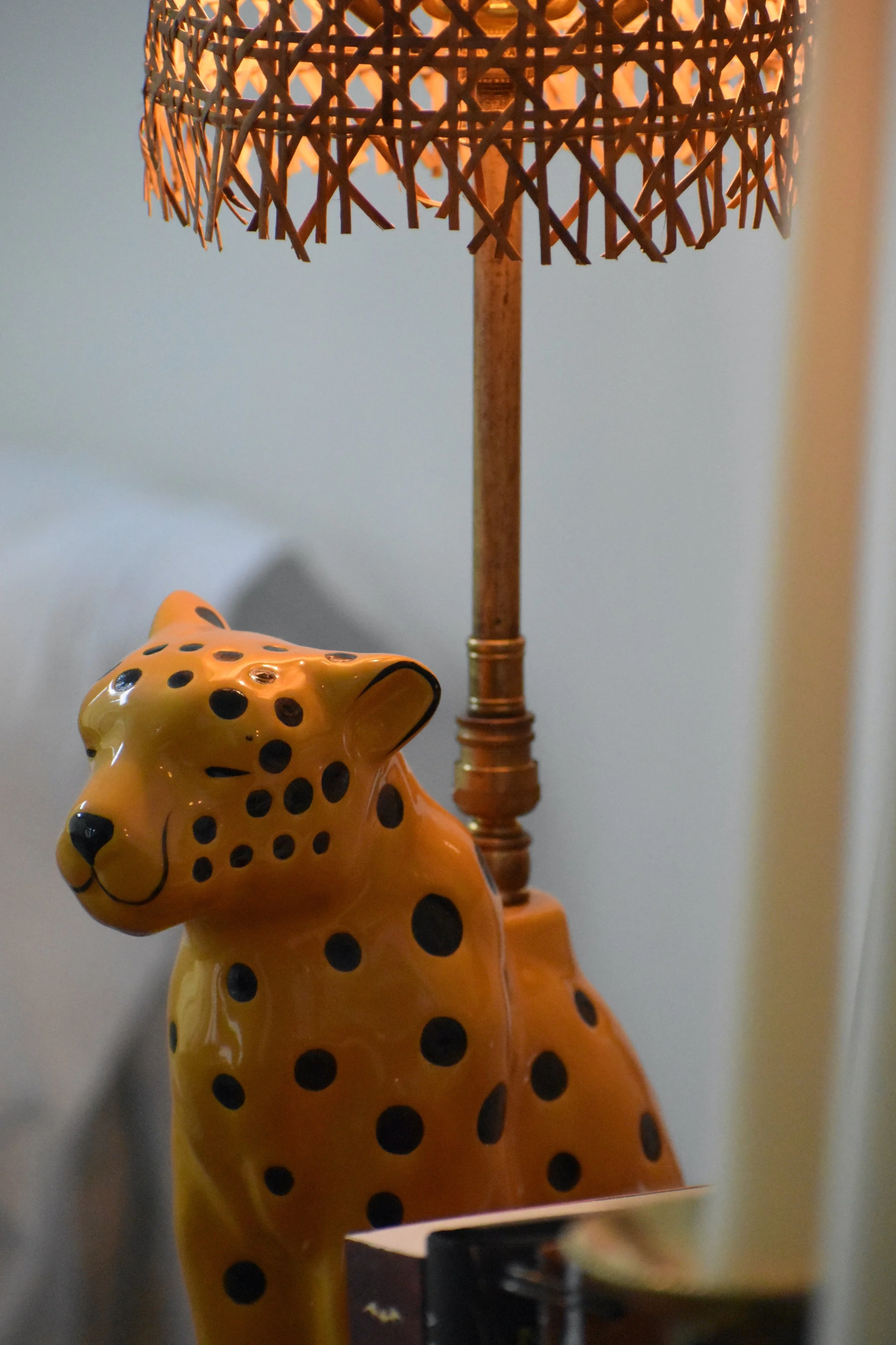 Yellow ceramic cheetah figurine with black spots placed beneath a woven rattan table lamp.