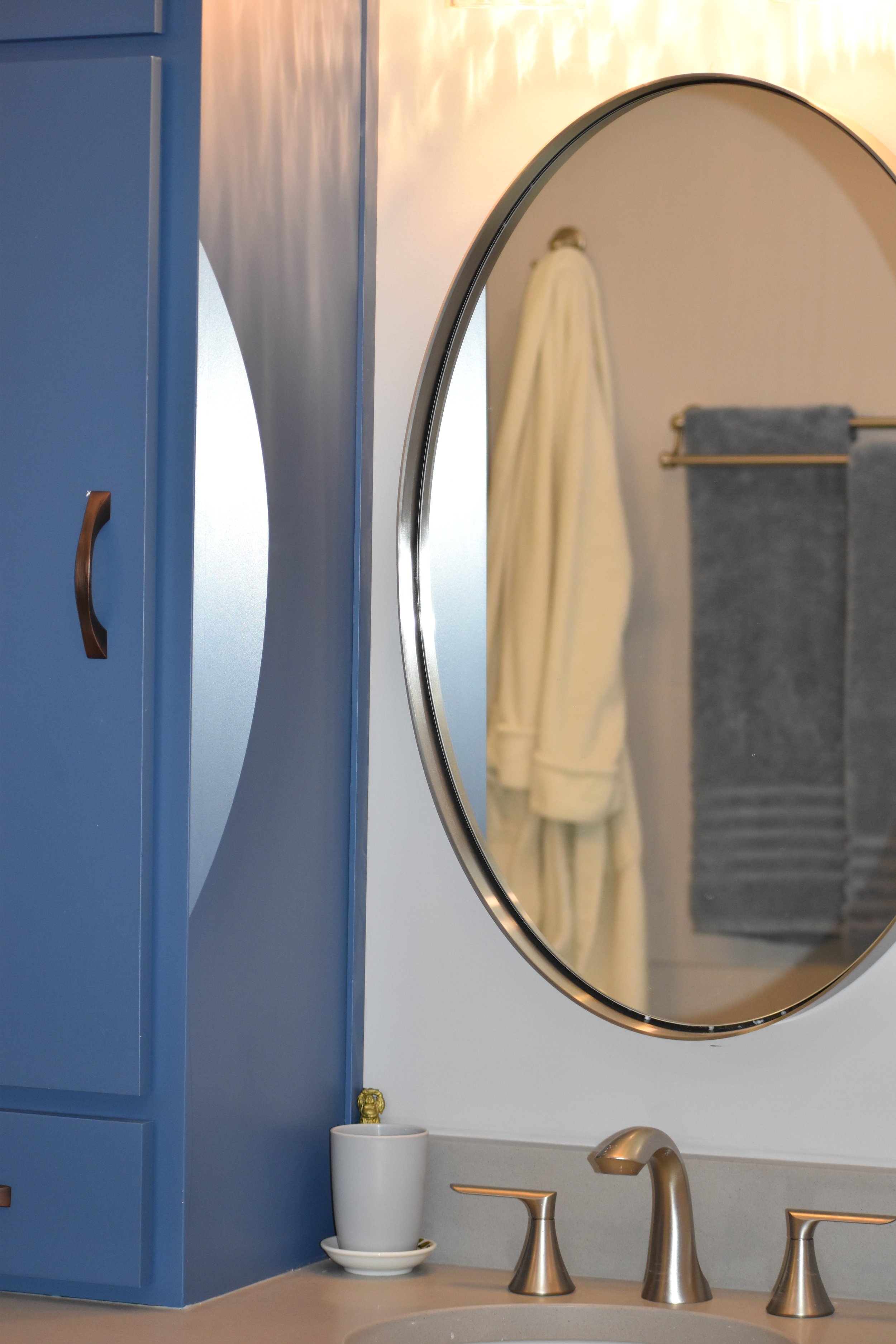 Bathroom with blue cabinet, round mirror, towel rack with gray towels, and a beige towel hanging, with a soap dispenser on the sink. Marietta GA bathroom remodel.