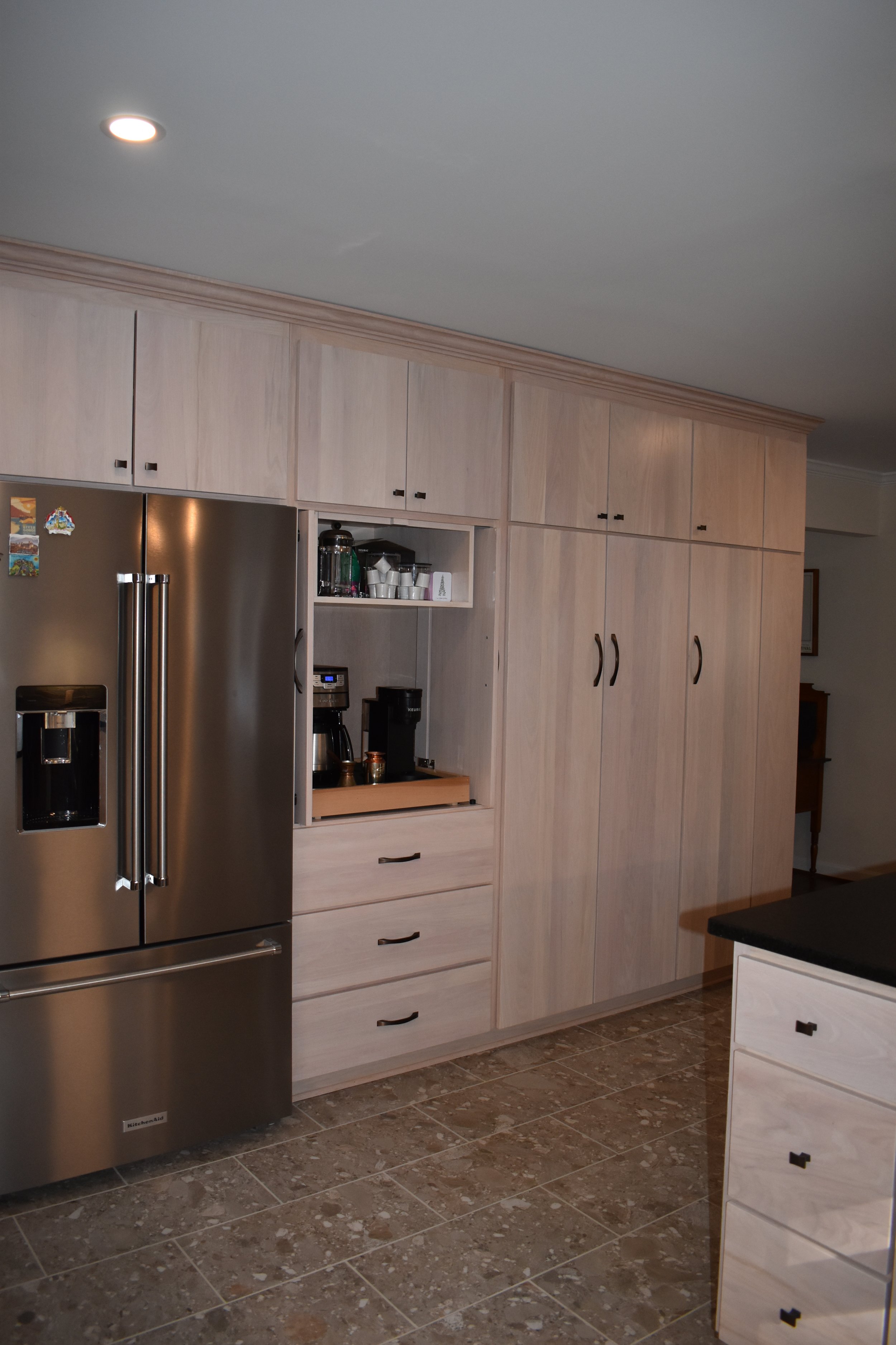 Kitchen with beige wooden cabinets, stainless steel refrigerator, black countertop, coffee maker, and tiled floor. Marietta GA kitchen remodel.