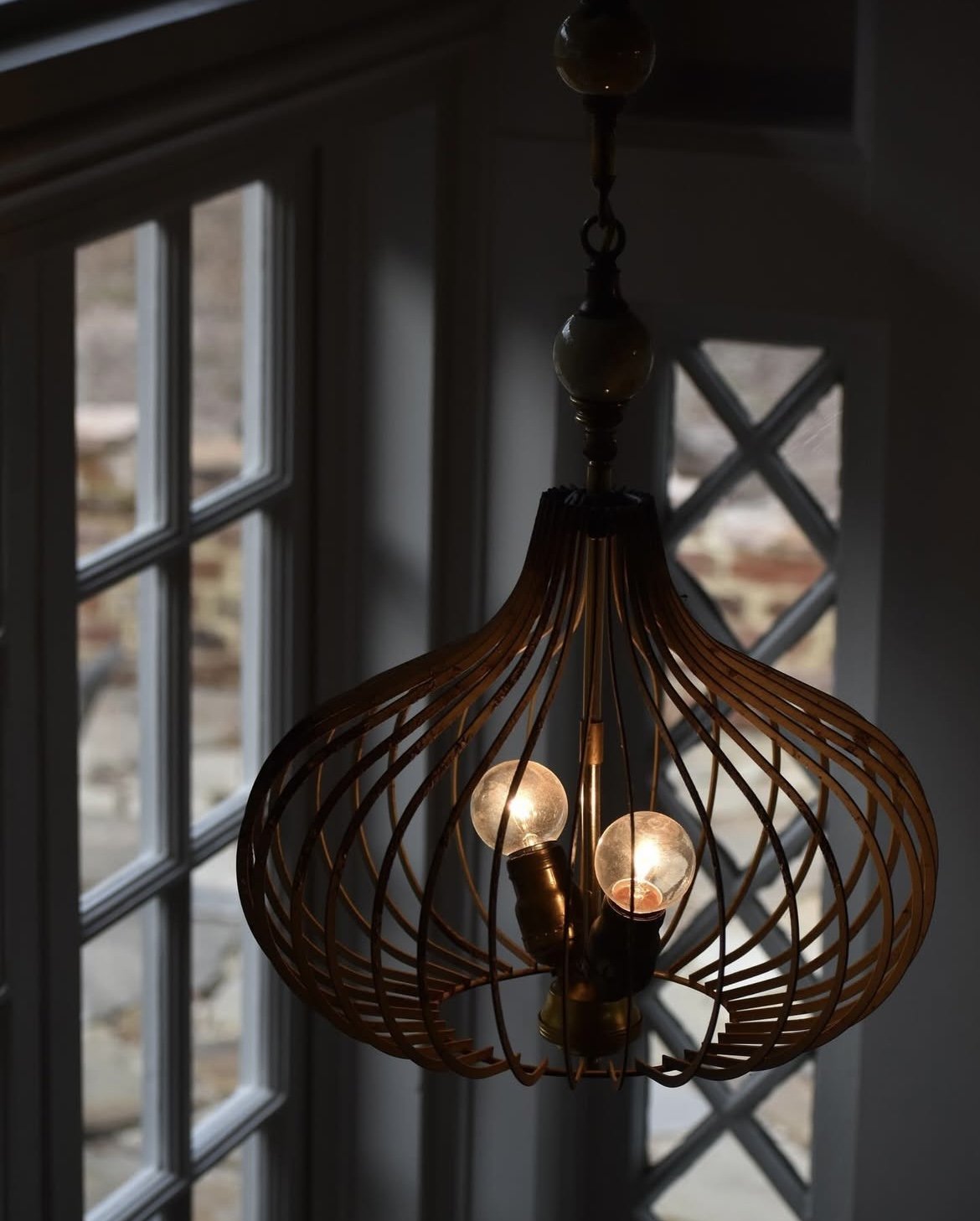 A pendant light fixture with a metal, open-weave design hanging in front of a multi-pane window inside a home. Custom Lighting