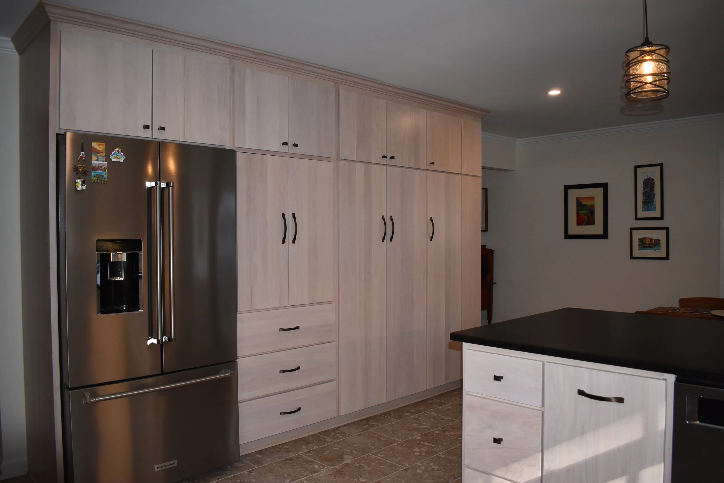 Modern kitchen with beige wooden cabinets, stainless steel refrigerator, dark countertop on island, tile floor, and artwork on the wall. Marietta GA kitchen remodel.