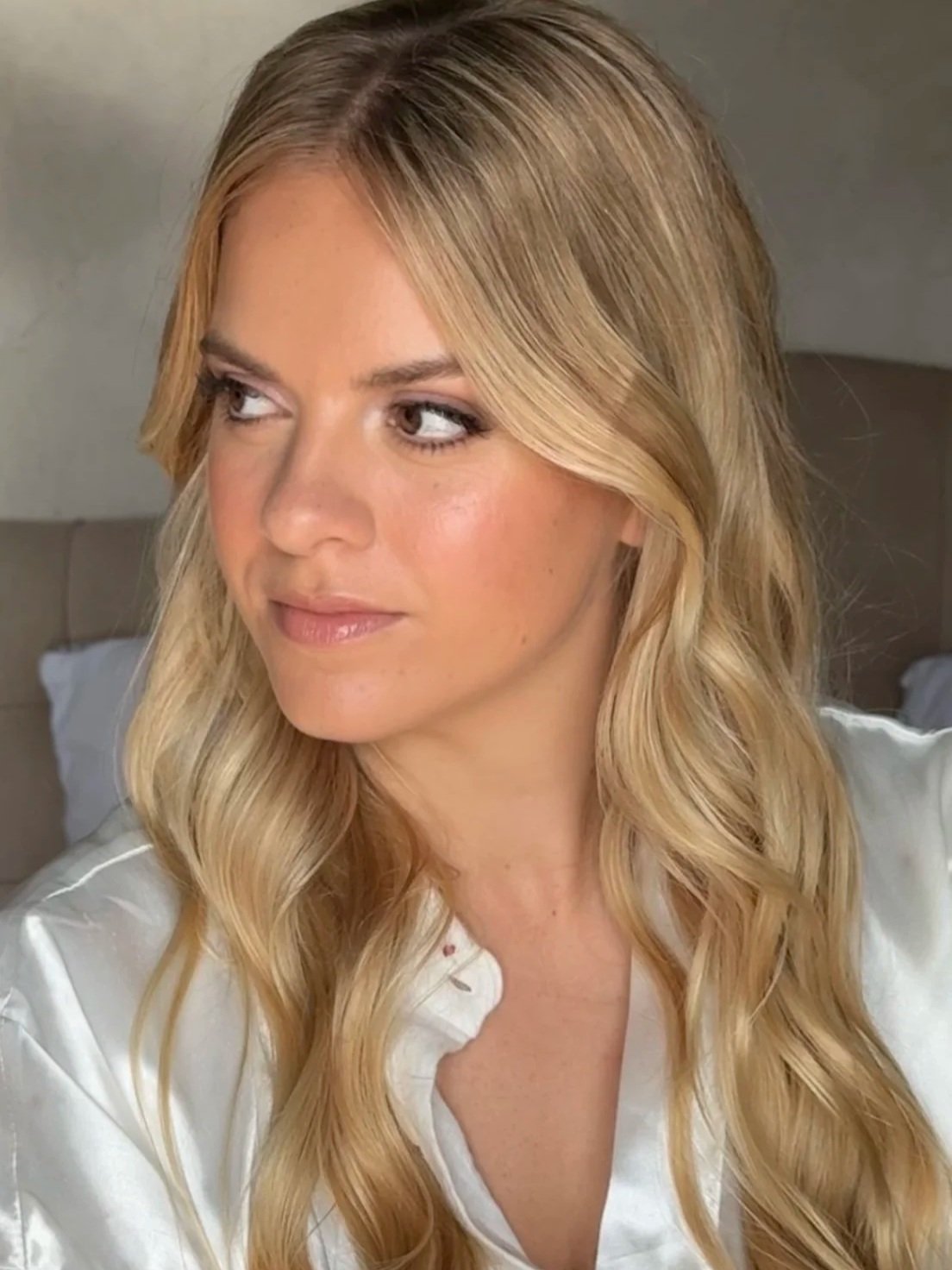 Close-up of a woman with blonde wavy hair wearing a white shirt, looking to the side.