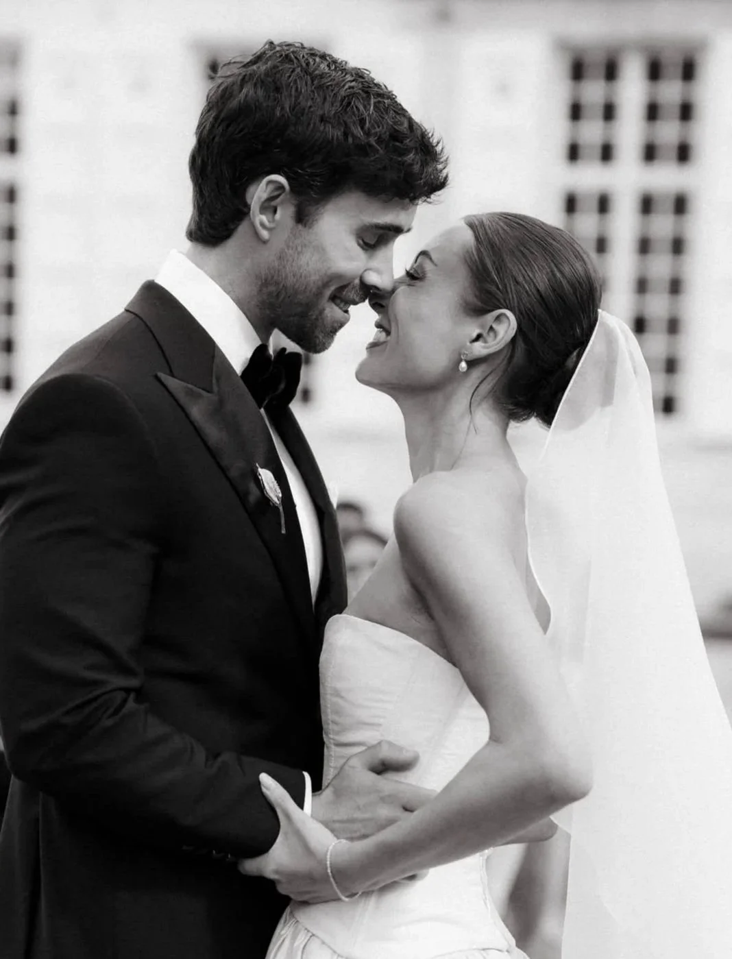 Black and white photo of a groom and bride close together, smiling and almost touching foreheads, on their wedding day.