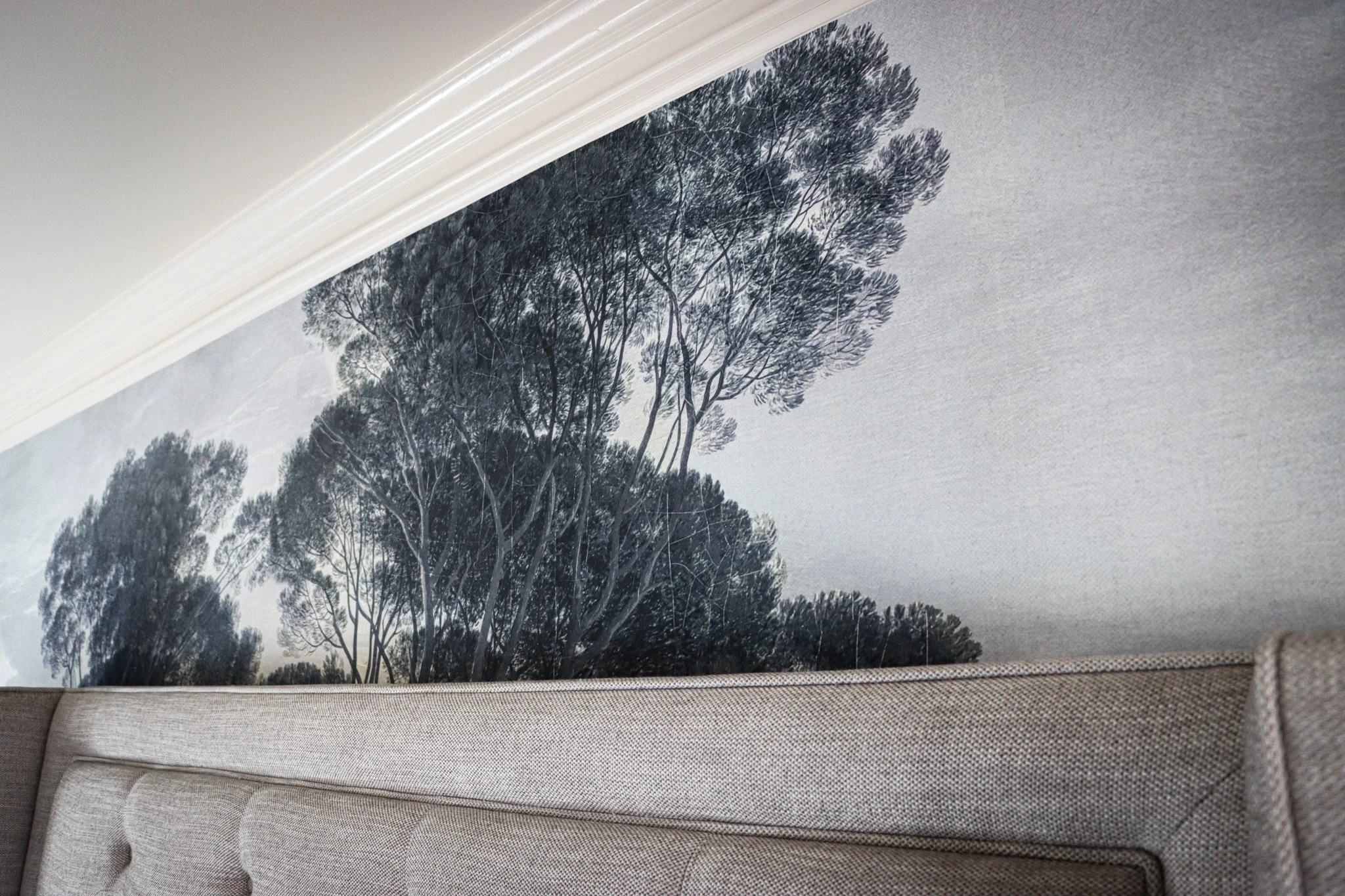 Room interior with a wall featuring a large black and white tree mural, a beige upholstered headboard, and white crown molding.