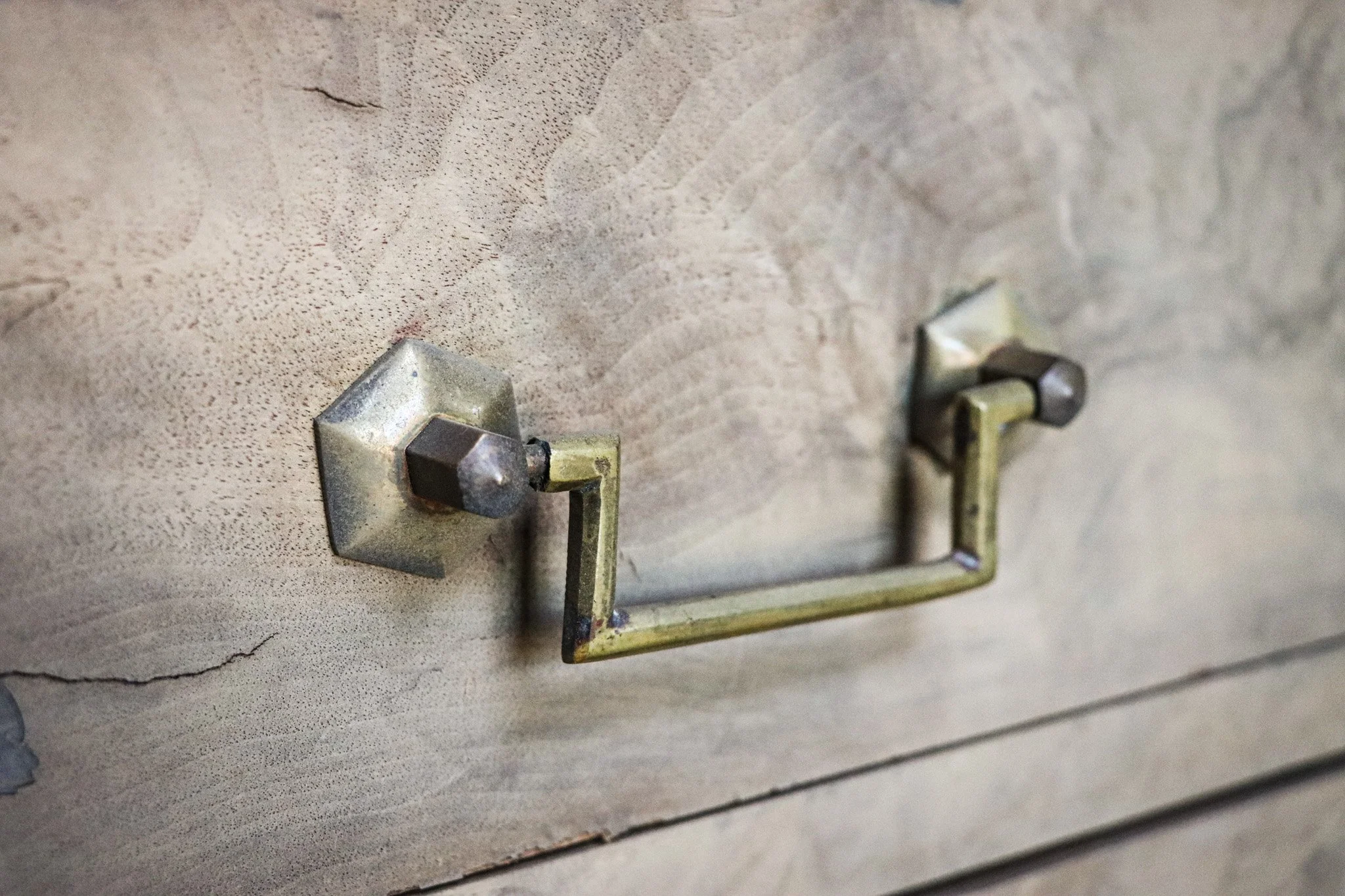 Close-up of a vintage metal drawer pull handle on a weathered wooden cabinet.