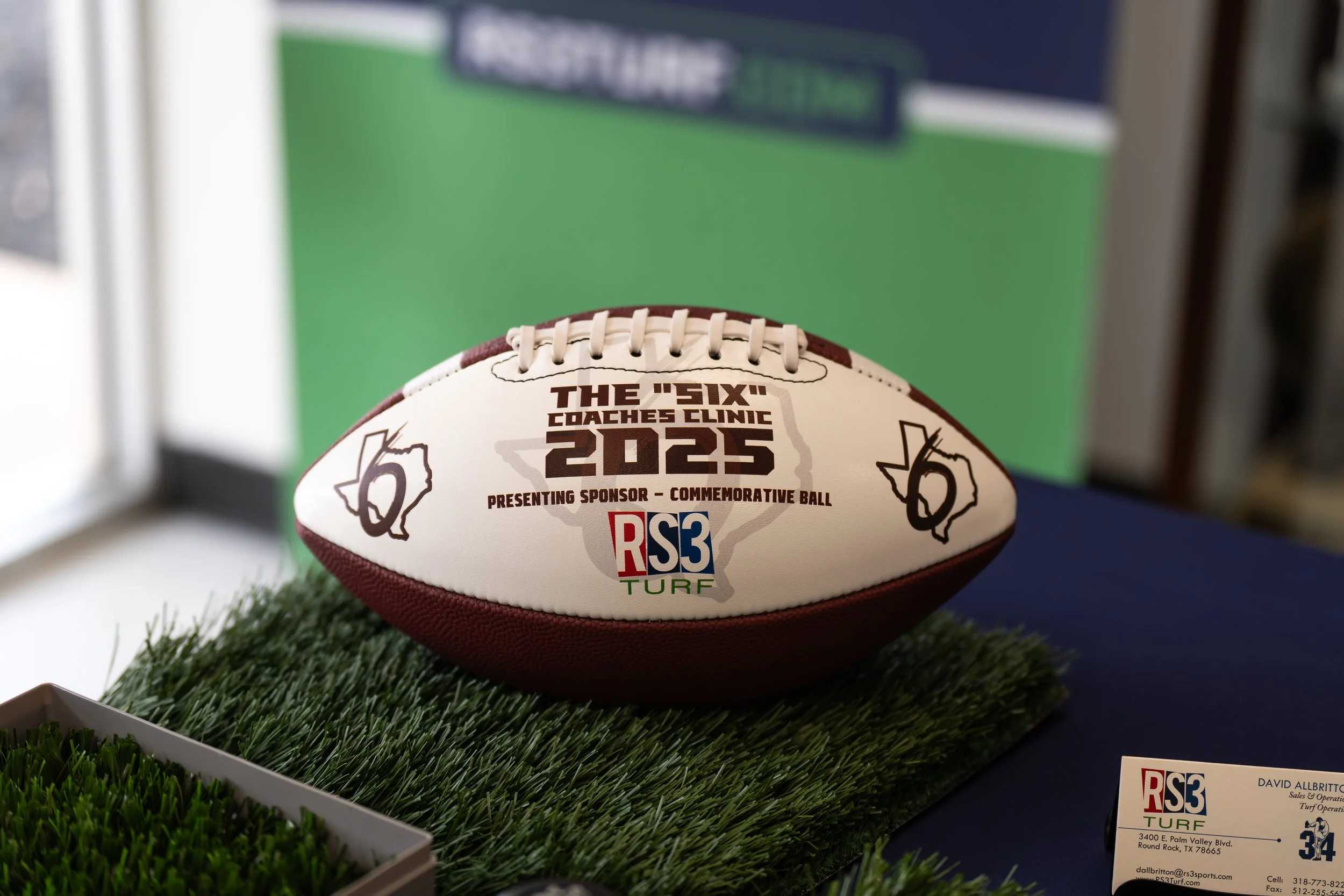 A commemorative rugby ball with text and logos, displayed on a patch of artificial grass at an event.