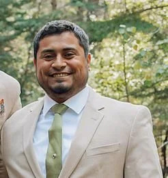 Smiling man in a beige suit and light green tie outdoors