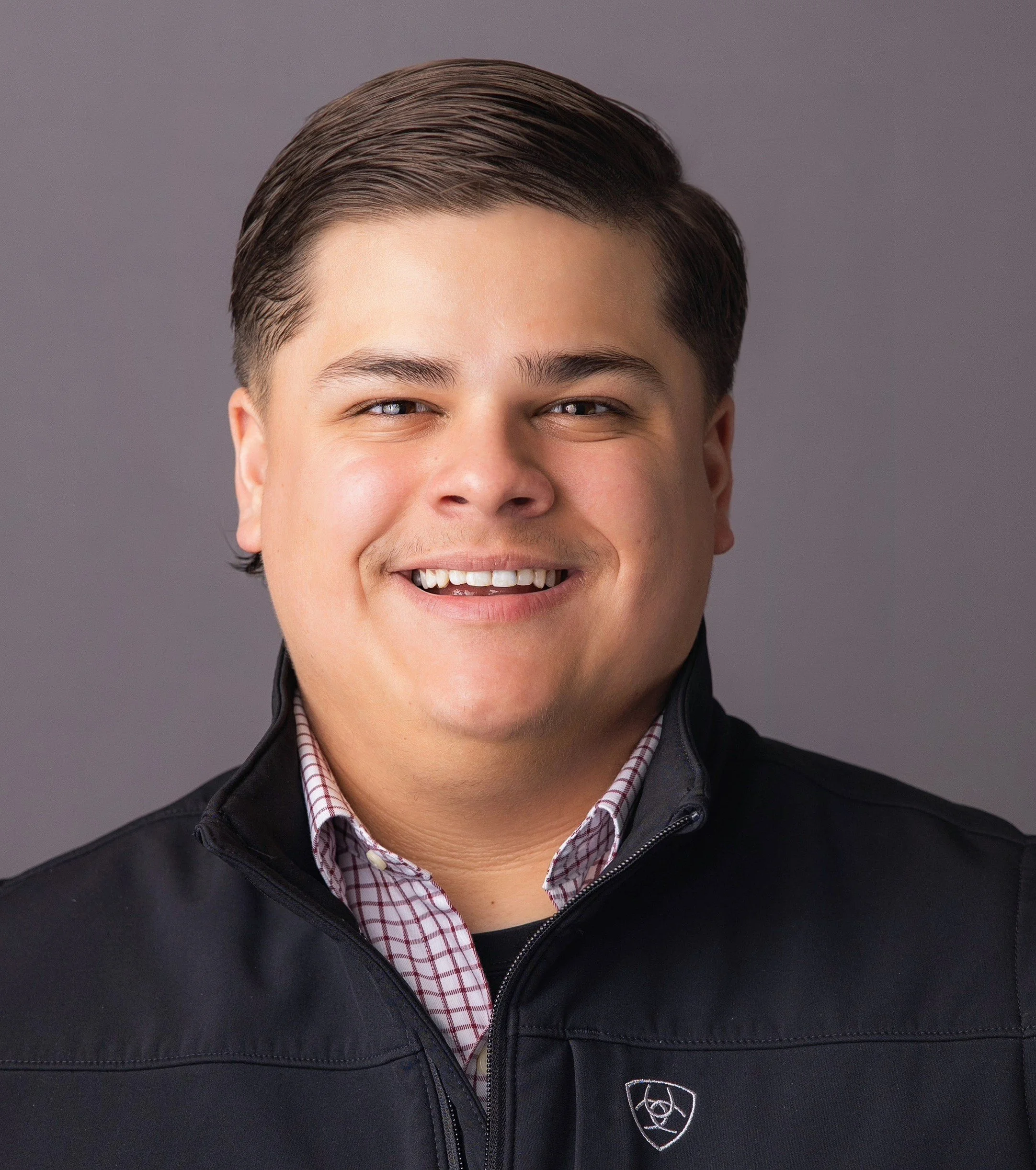 Portrait of a young man smiling in a blue jacket against a gray background.