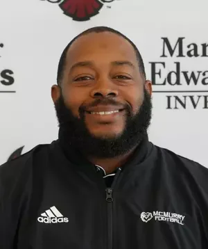 Portrait of a man with a smile, short hair, and beard, wearing a black Adidas jacket, standing in front of a backdrop with text related to McLeroy Football and Montgomery Edwards.