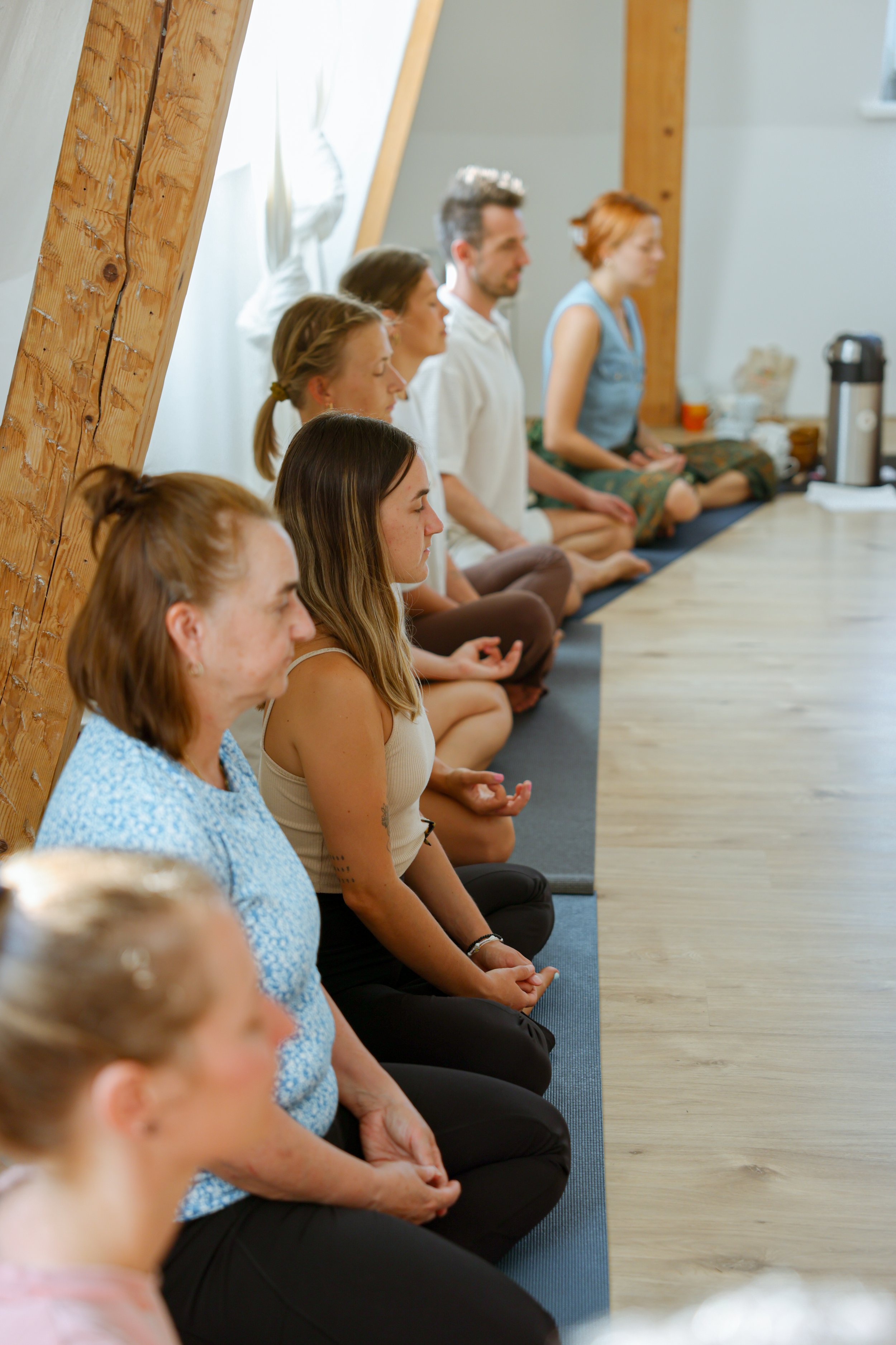 Menschen, die im Schneidersitz auf Yogamatten im Raum sitzen, bei einer Meditation oder Achtsamkeitsübung.