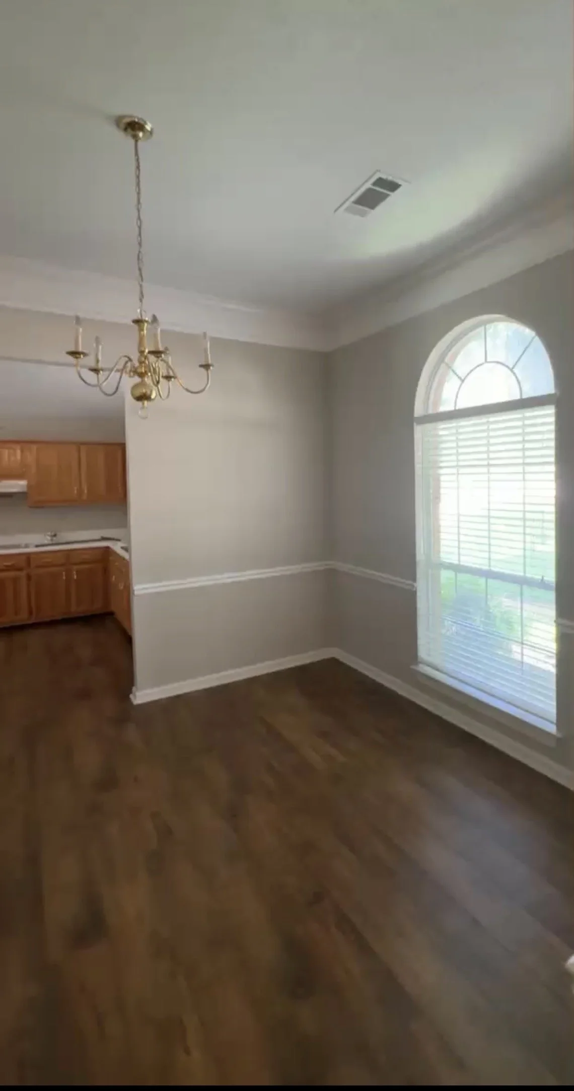 Empty dining area with hardwood floors, a chandelier, and a large arched window with blinds in a home.
