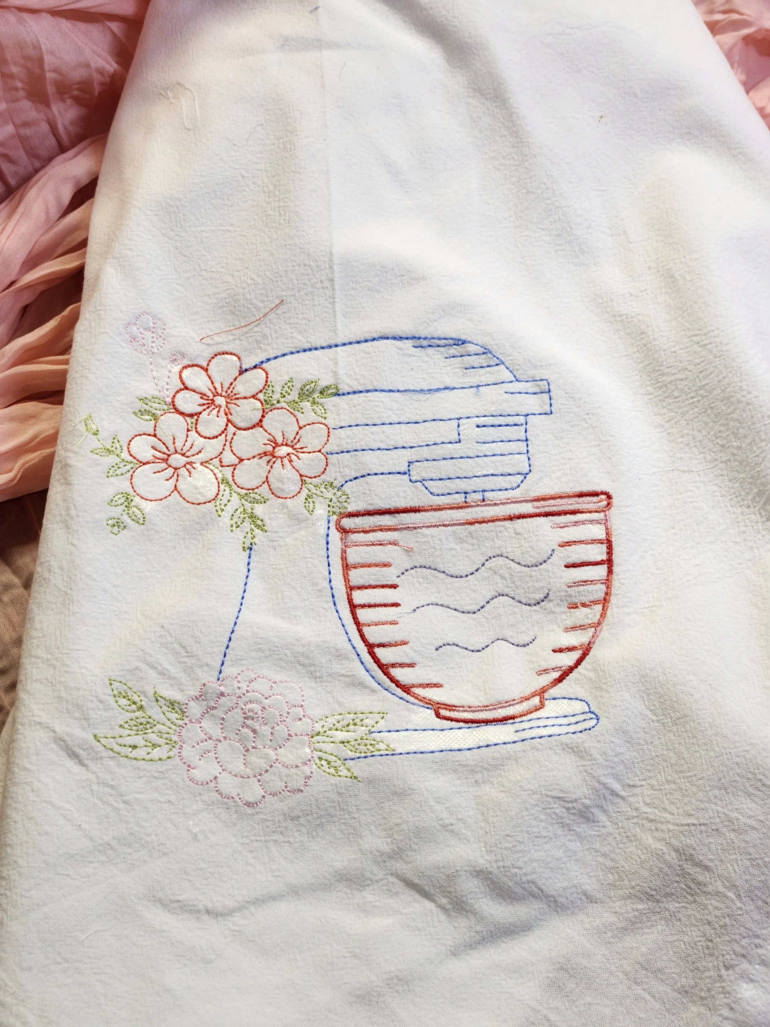 Embroidery of a stand mixer with flowers on a white fabric.