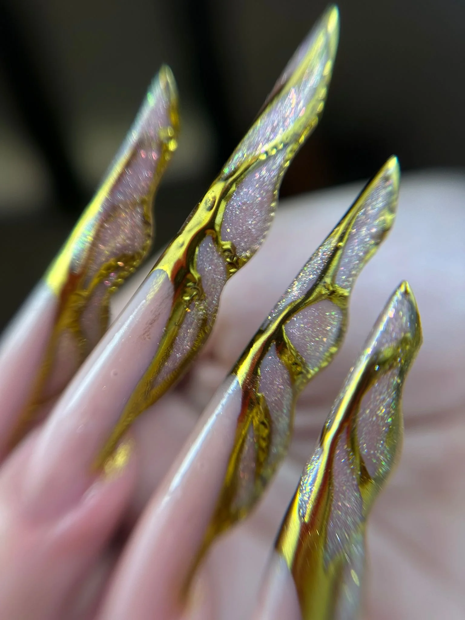 Dettaglio di unghie finte con decorazioni dorate e iridescenti, molto decorate e lucenti.