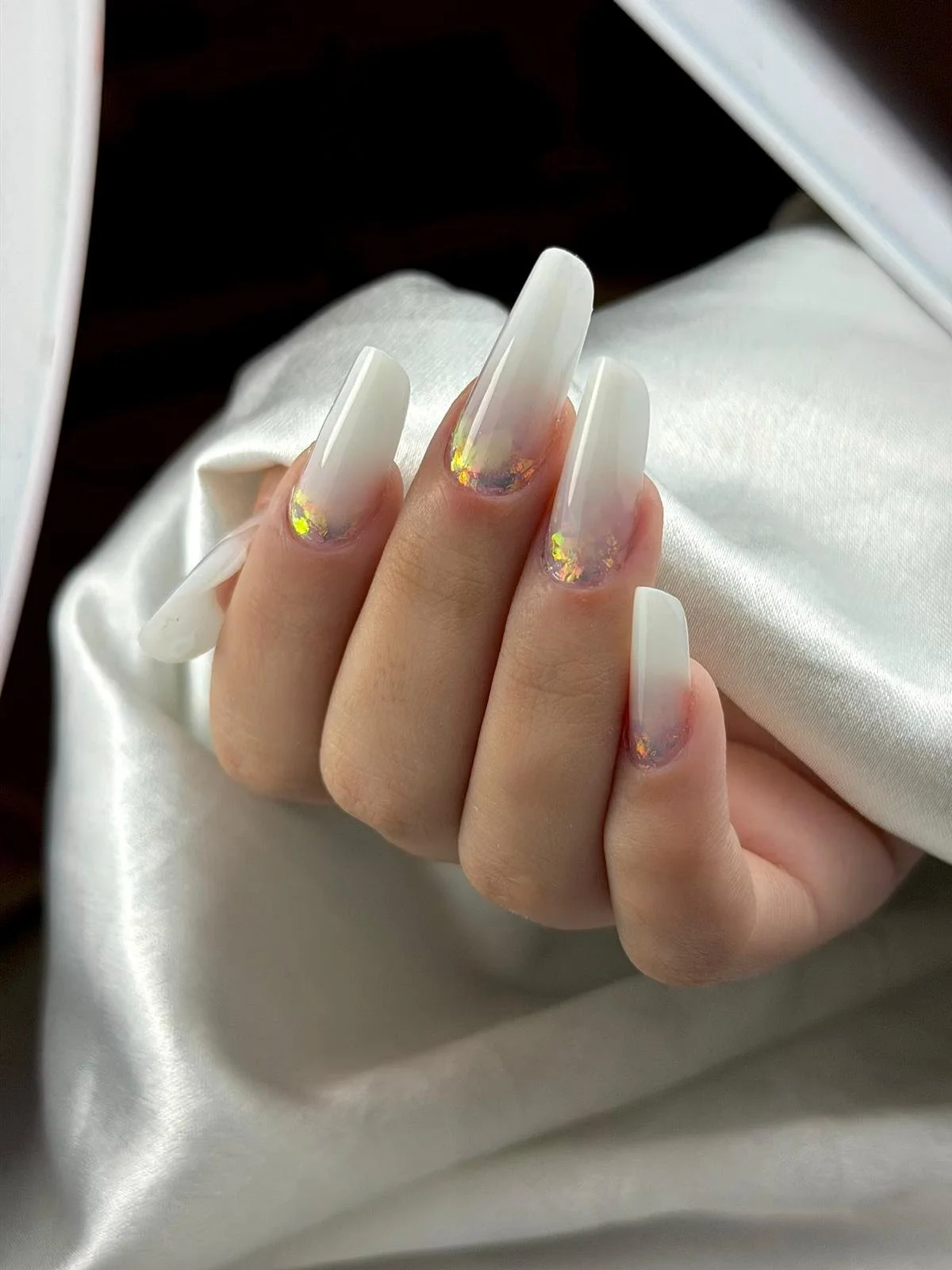 Unghie con decorazioni di French manicure e dettagli di glitter dorati, mani che riposano su un tessuto bianco.