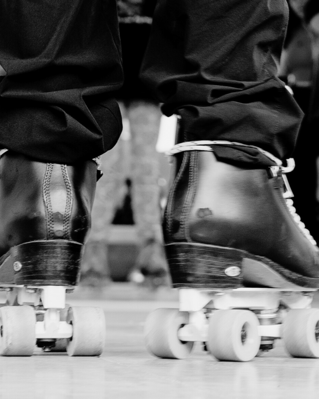 Close-up of roller skates worn by two people, with their legs and feet visible, on a rink floor.