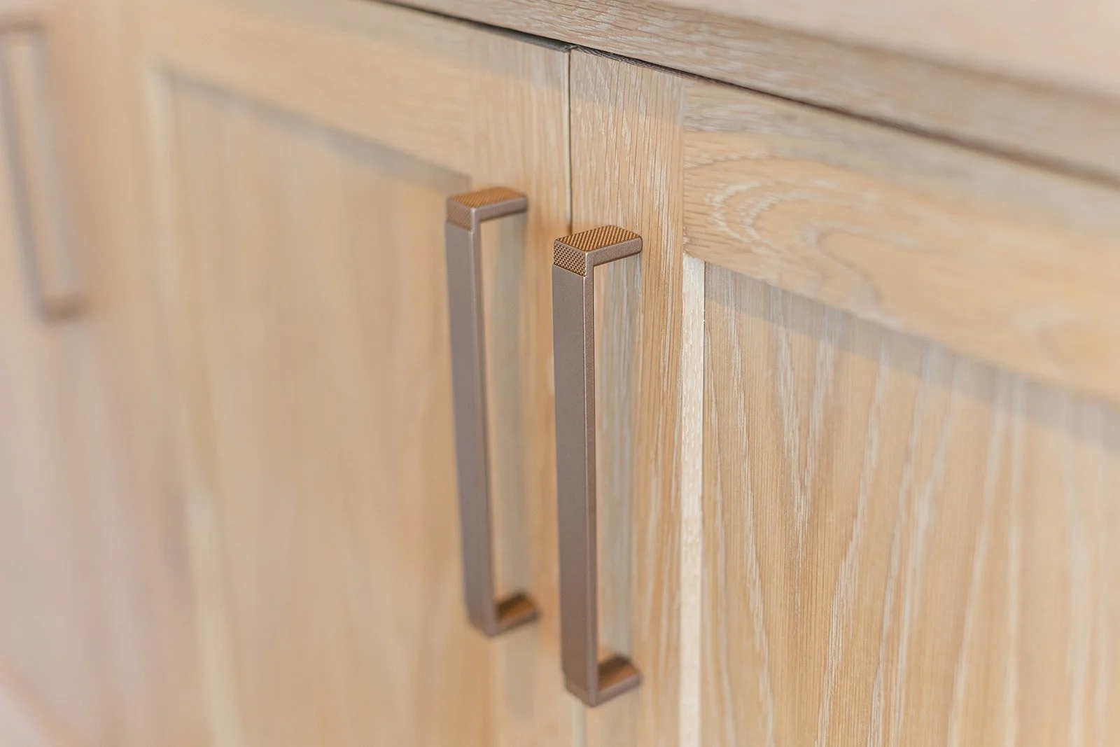 Close-up of two brushed metal cabinet handles on light wood cabinet doors.