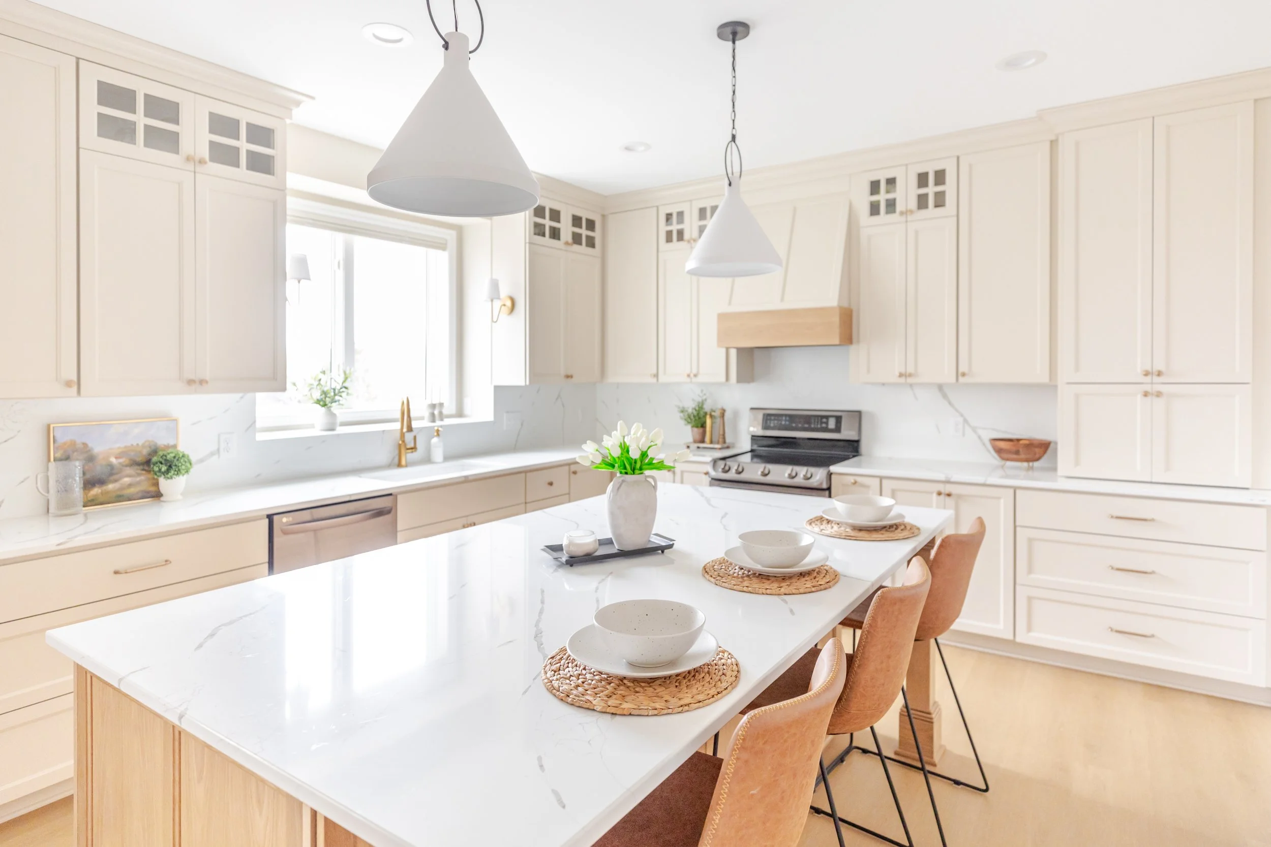 Bright kitchen with white cabinets and marble countertops, kitchen island with place settings, and window with a view outside.