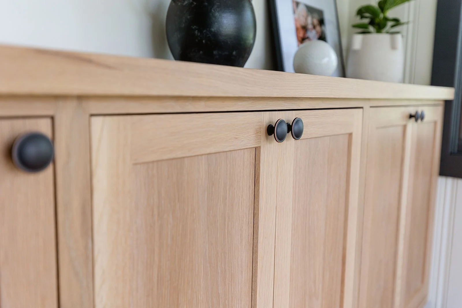 A wooden sideboard with round black knobs, decorated with vases and picture frames on top.