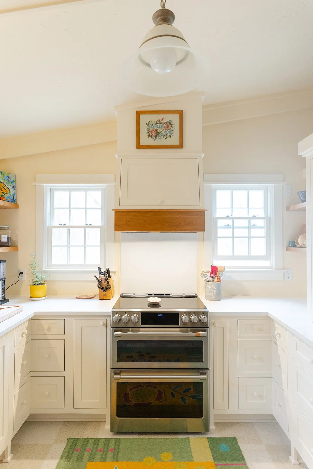 Bright kitchen with white cabinets, stainless steel oven, two windows, and decorative items on countertops.