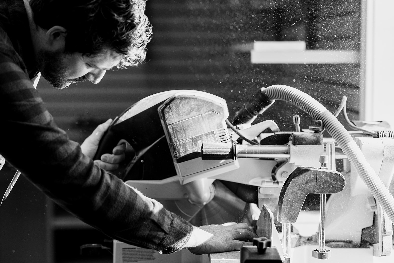A man operating a large industrial machine, likely a saw, in a workshop, with sawdust flying around.