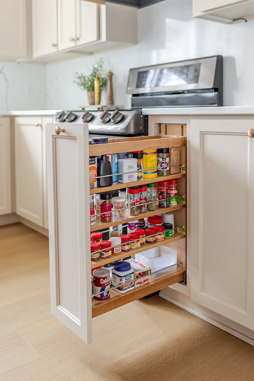 Open kitchen cabinet drawer filled with spices and seasonings such as garlic powder, basil, and red pepper flakes.