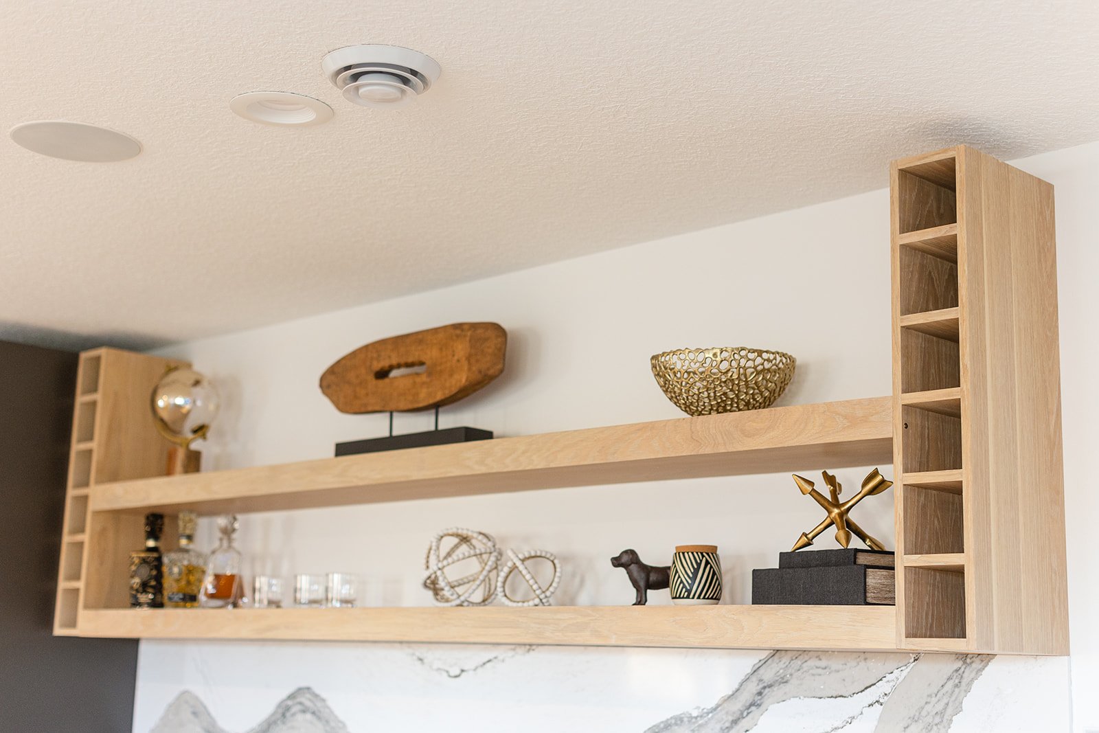 Wooden wall shelf with decorative items such as a bowl, sculpture, and small figurines mounted on a wall above a marble surface.