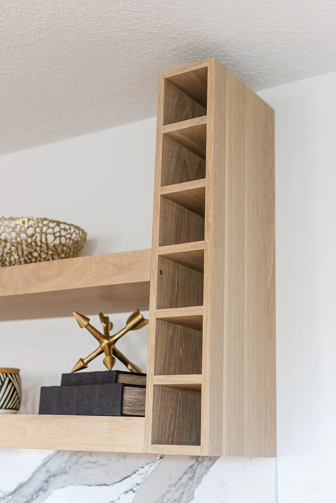 Close-up of a wooden wall-mounted shelf with a small open compartment on the right and a flat surface on the left, decorated with a woven bowl, a decorative sculpture, and a black book.