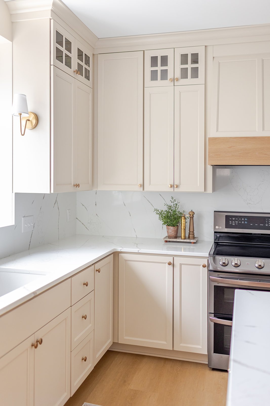 White kitchen cabinets with gold knobs, marble countertops, a potted plant, and a stainless steel stove.
