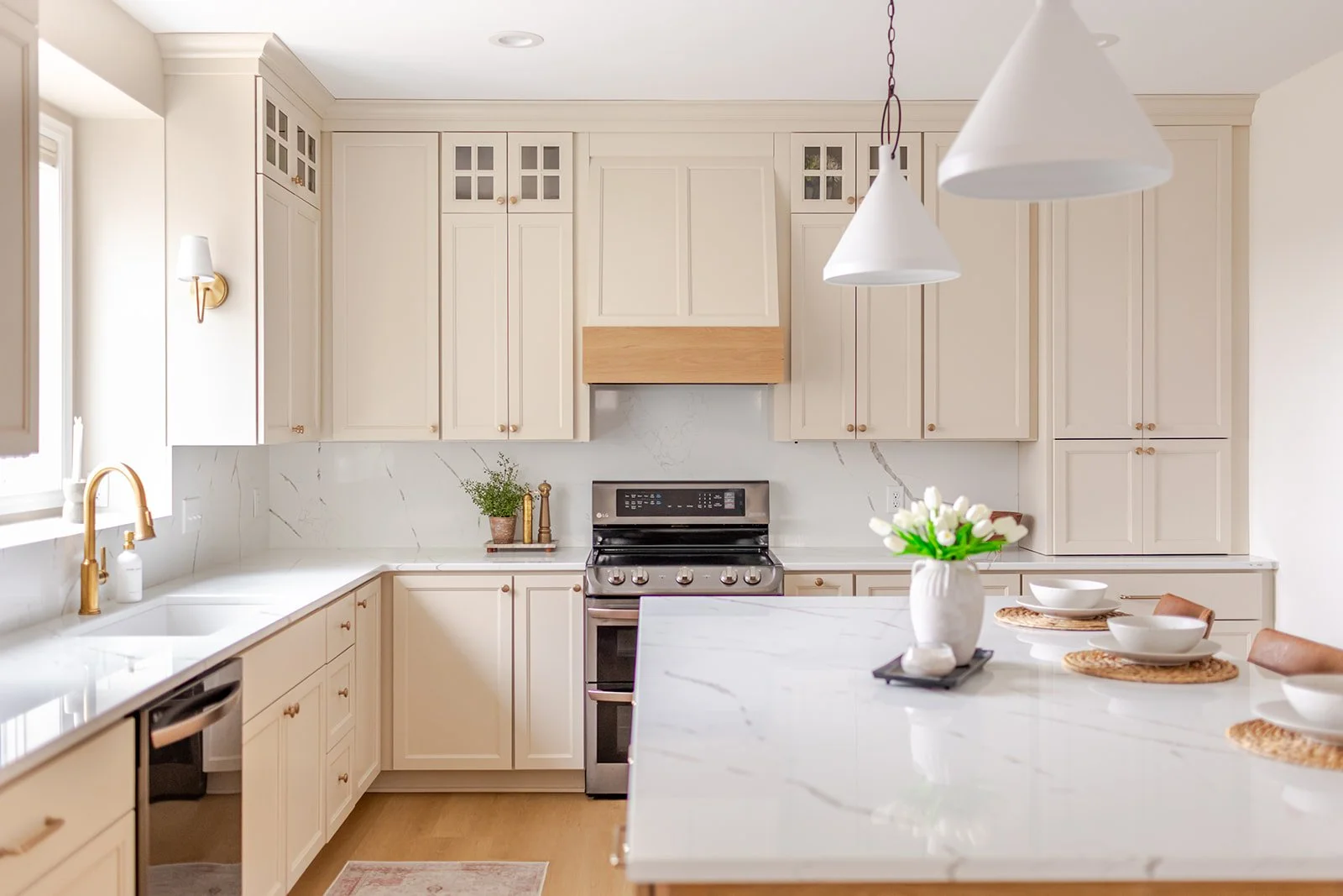 A modern kitchen with white cabinets, a marble backsplash, a stainless steel stove, a kitchen island with white marble countertop, plants, and white tableware with placemats