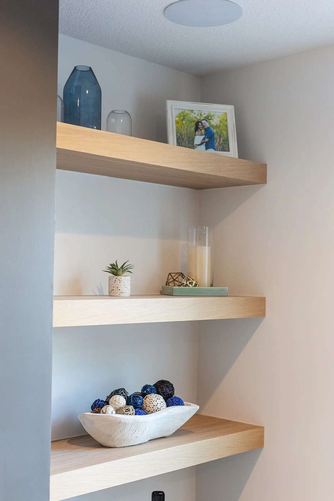 Decorative wall shelves with vases, a framed photograph, a small plant, candles, and decorative balls.