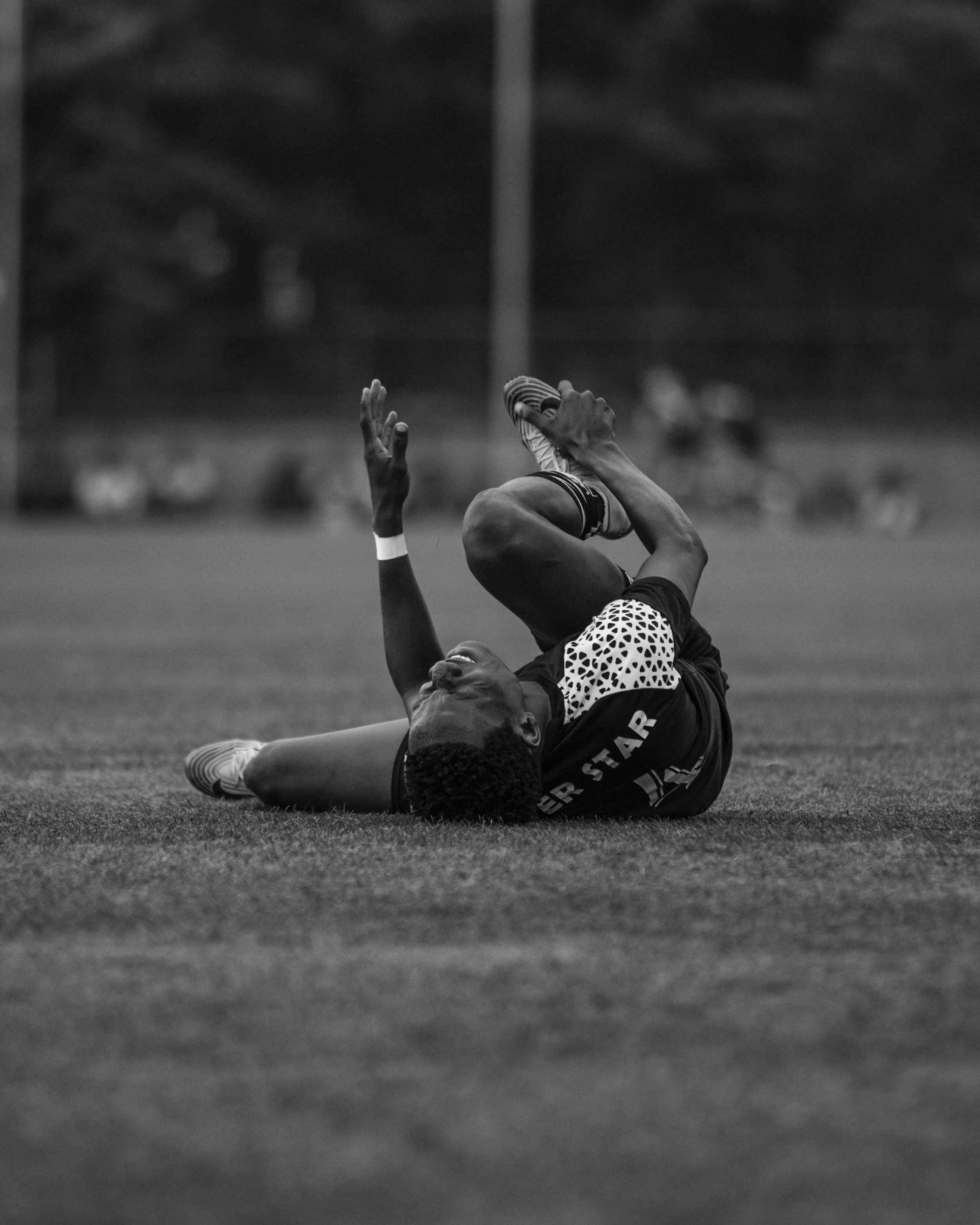 A soccer player is lying on the ground holding his leg in pain during a game at a sports field.