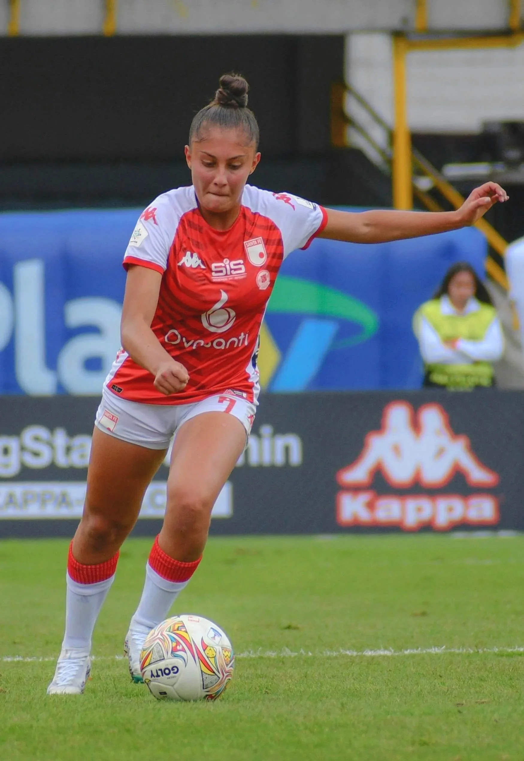 A female soccer player in a red and white uniform preparing to kick a soccer ball on a grass field during a game.