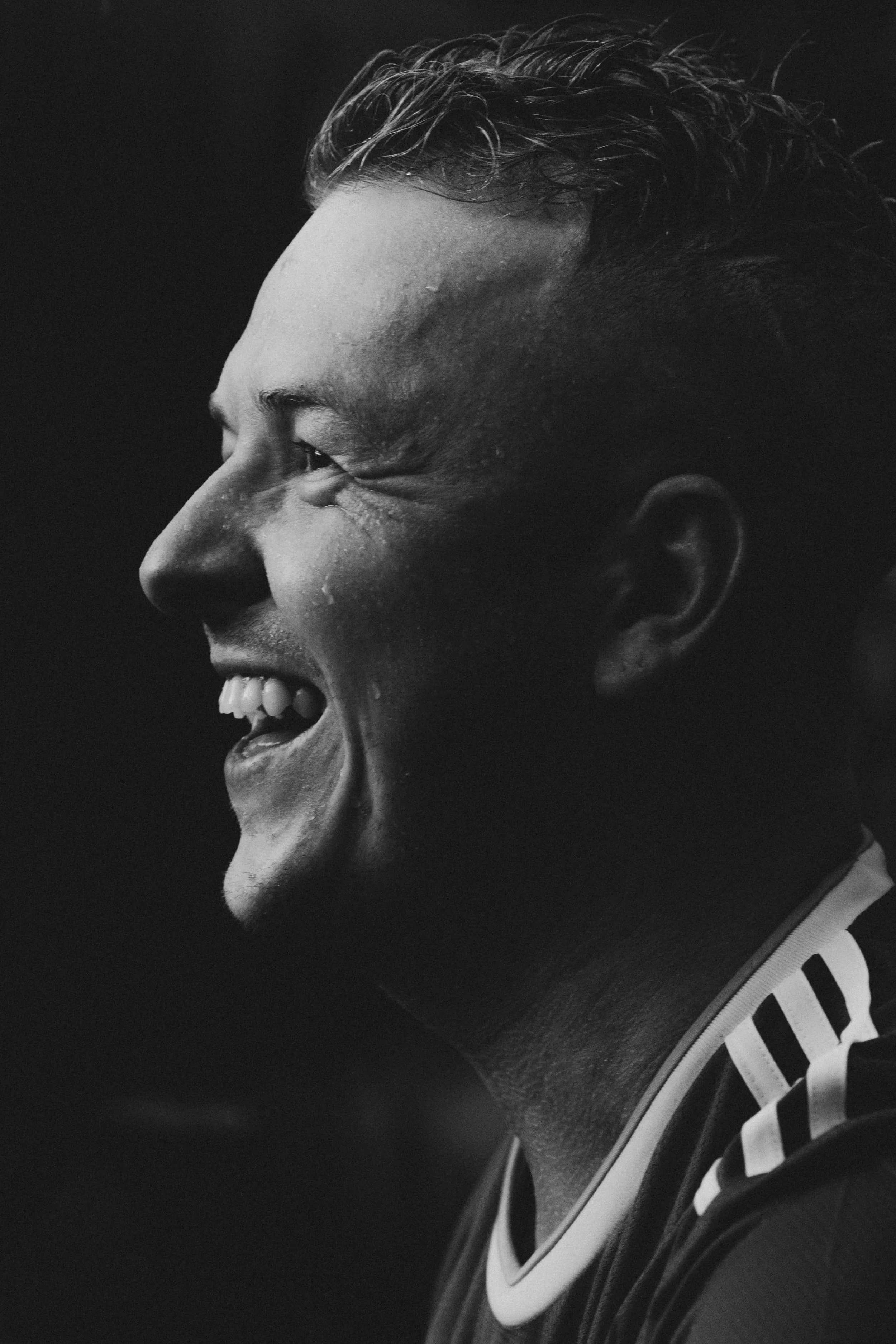 Black and white close-up of a smiling man with water droplets on his face.