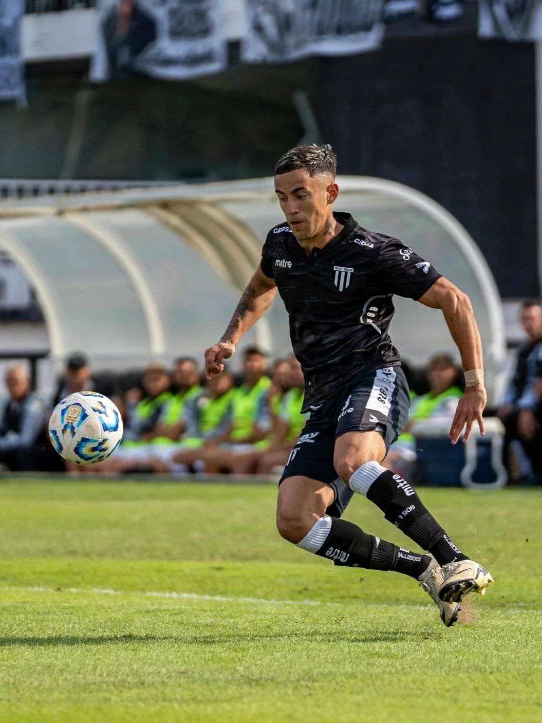 A soccer player in a black uniform chasing a soccer ball on the field during a match.