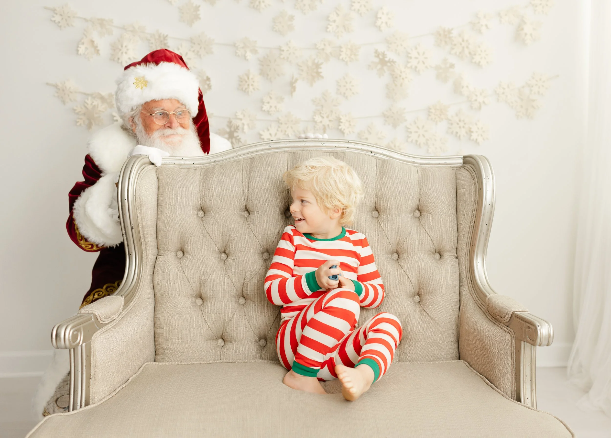 Santa playfully peeking over the settee at a laughing child during a private Santa session