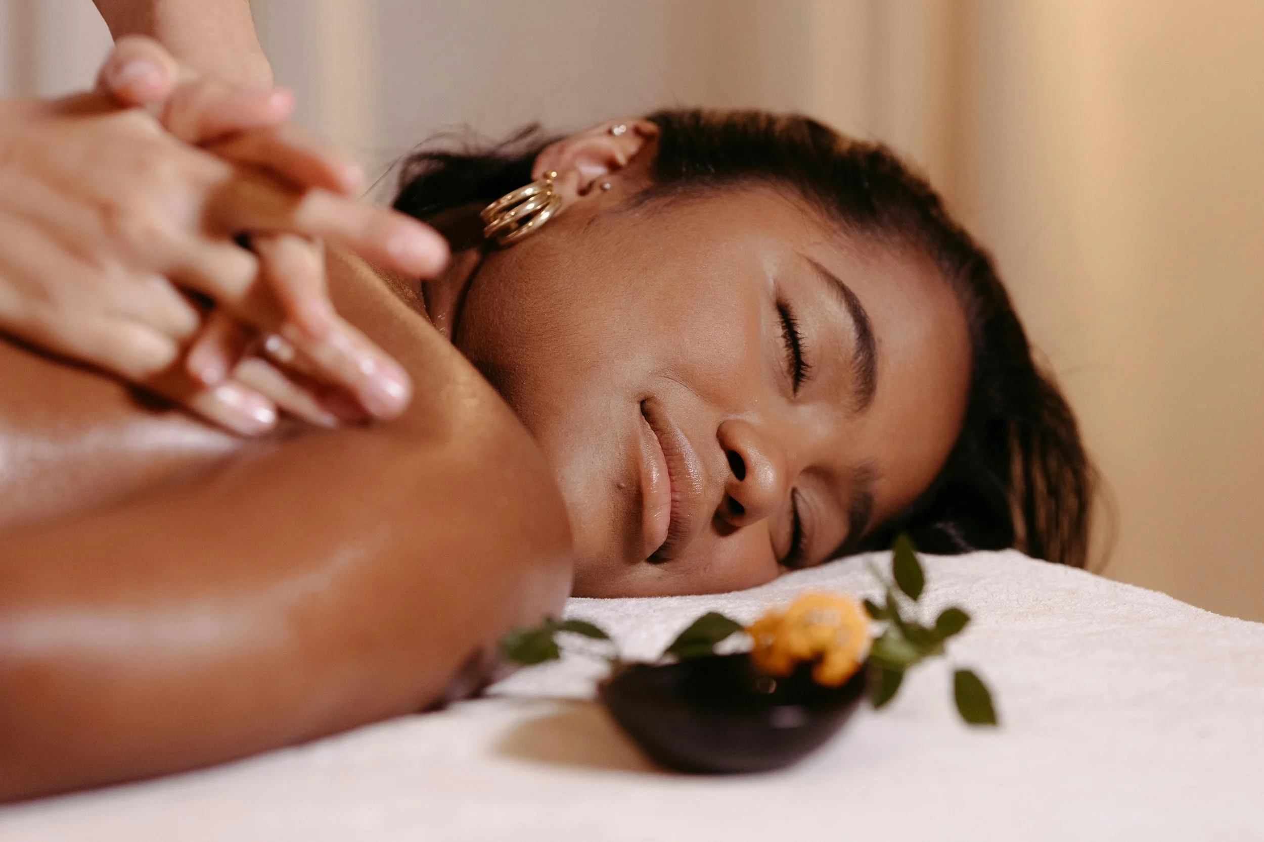 Woman lying on a massage table receiving a massage, with flowers in a small bowl nearby.
