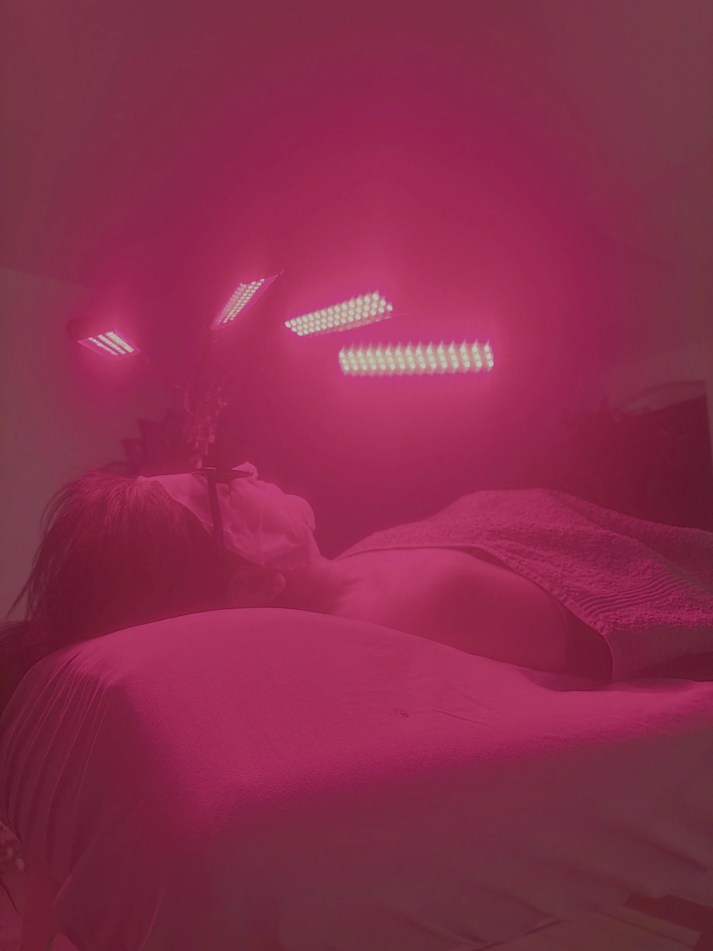 Person lying on a bed with a towel, illuminated by pink LED lights creating a vibrant glow.