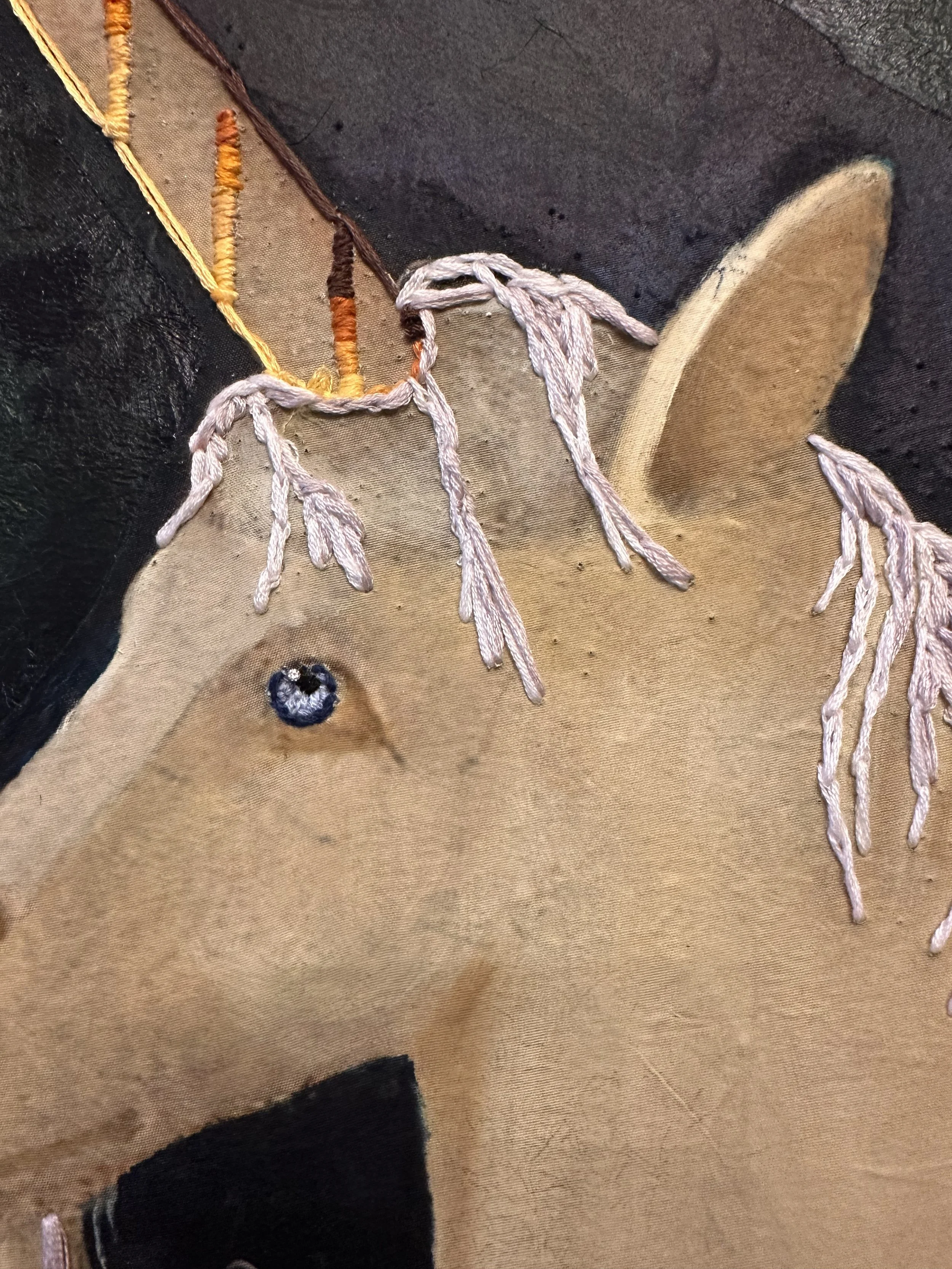 Close-up of embroidery of the unicorn's forelock, horn, and mane, featuring the eye with the diamond and embroidery silk.
